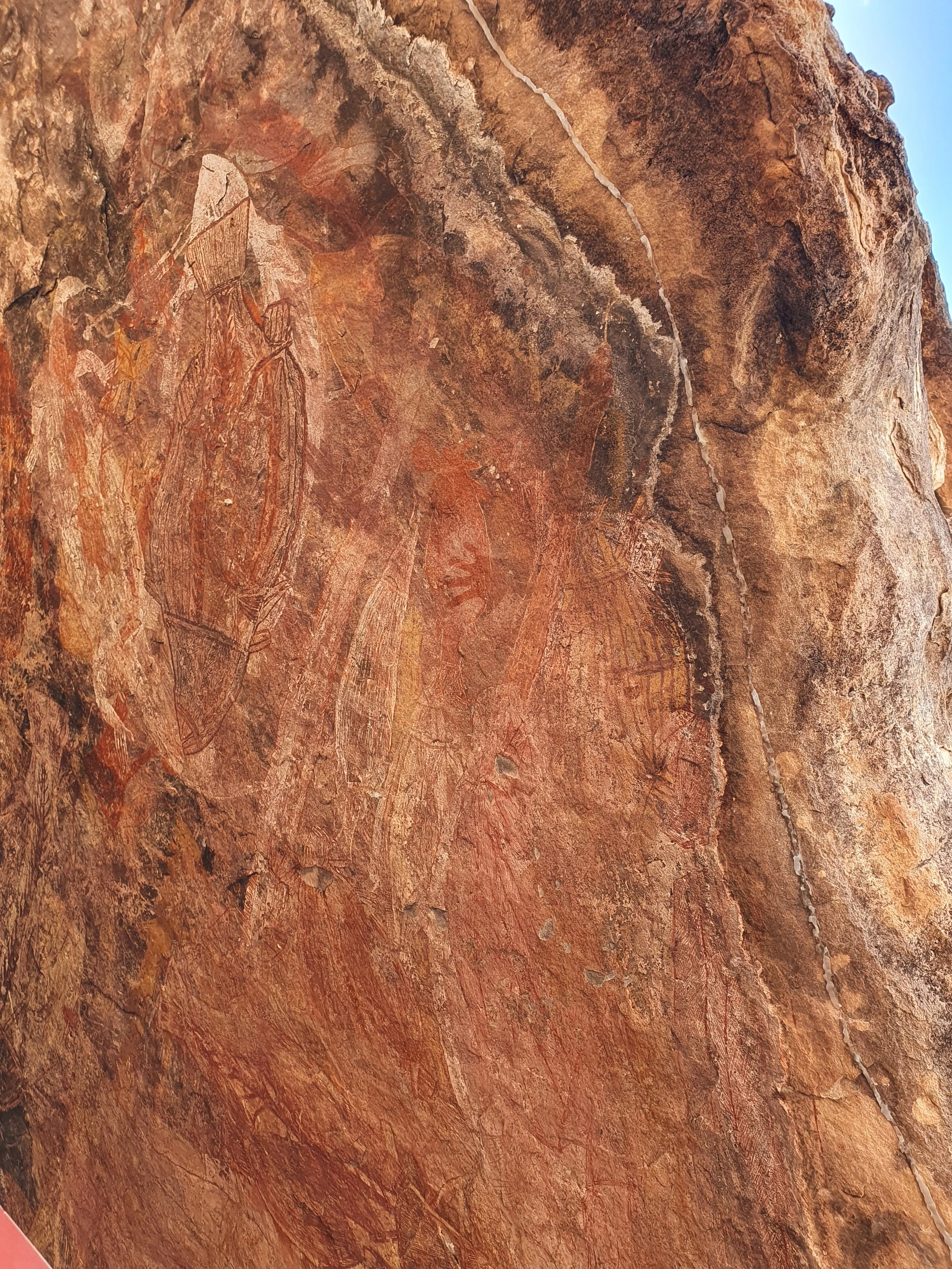 Cave etchings depicting animals, including a large insect and a mammoth, carved into a reddish-brown stone wall.