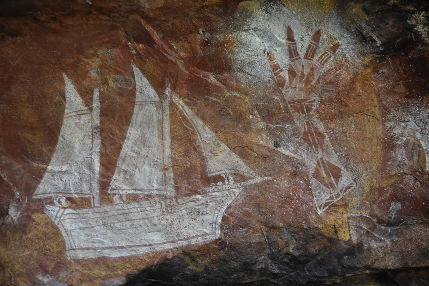 Prehistoric cave paintings of boats, a human face with a headdress, and other figures on a rock surface.