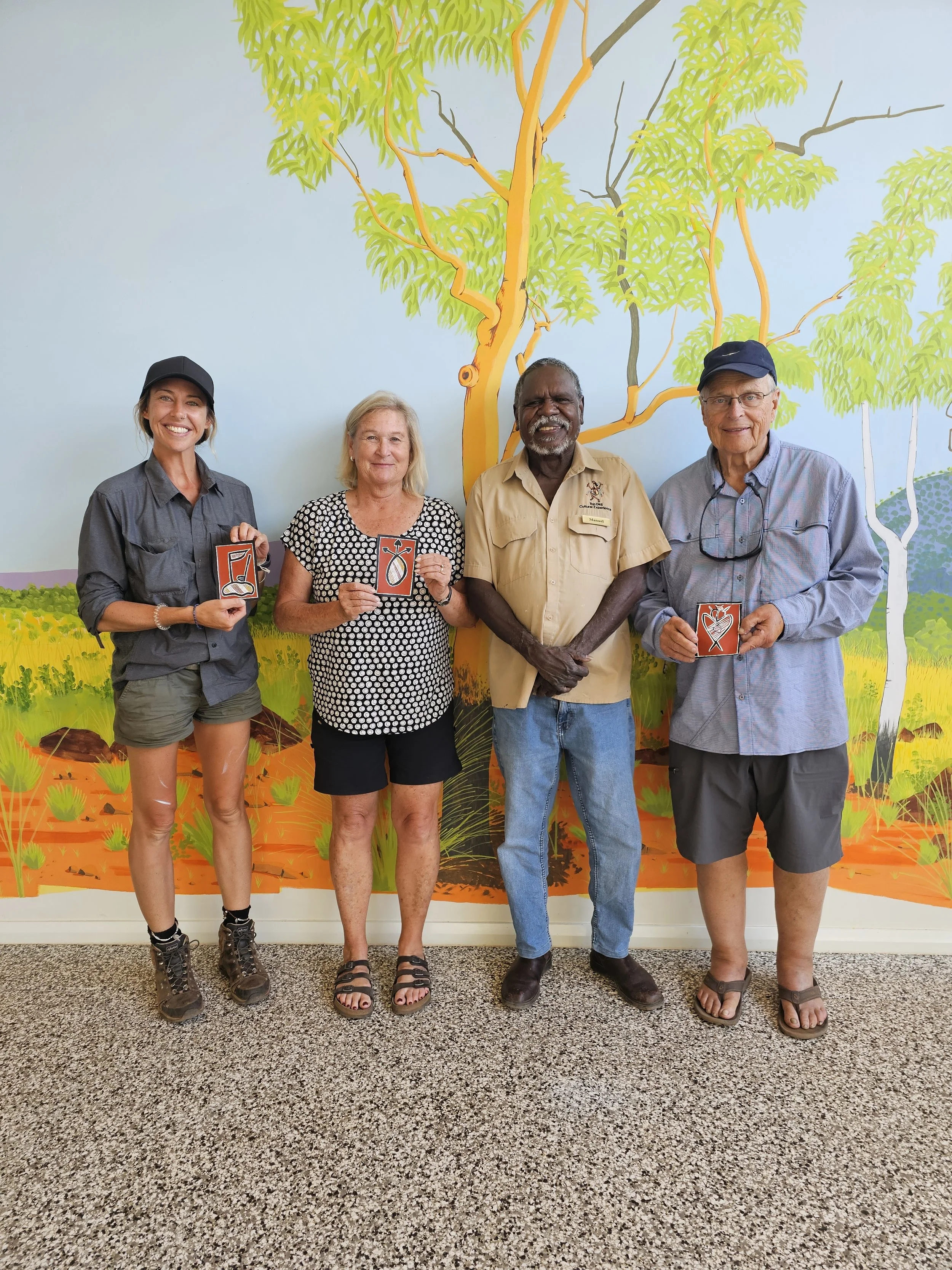 Four people standing in front of a colorful mural and holding small cards with heart and health-related symbols.