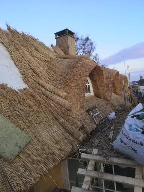 Et tag med stråbelægning, der er under opbygning, med nogle værktøjer og materialer rundt om.