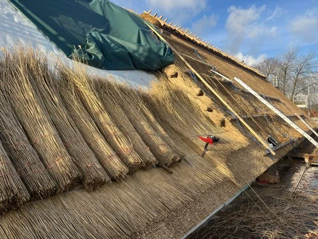 Et skråt billede af en tagkonstruktion under reparation, med værktøj og materialer, herunder en varmepistol, på taget. Tækkemand Nordsjælland Furesø Tækkeentreprise ApS