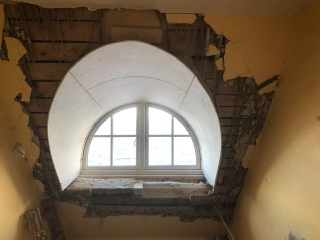 Vindue i en væg under renovering, omgivet af delvist fjernet væg og synlige bygningsmaterialer.