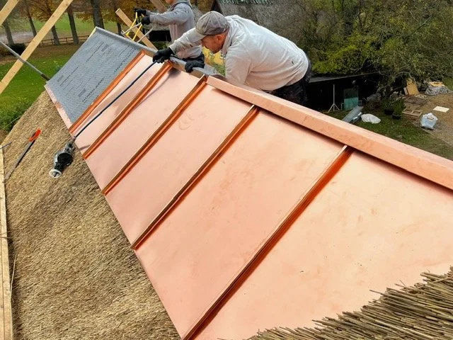 To personer arbejder på tagdækning med kobberplader på et taget.