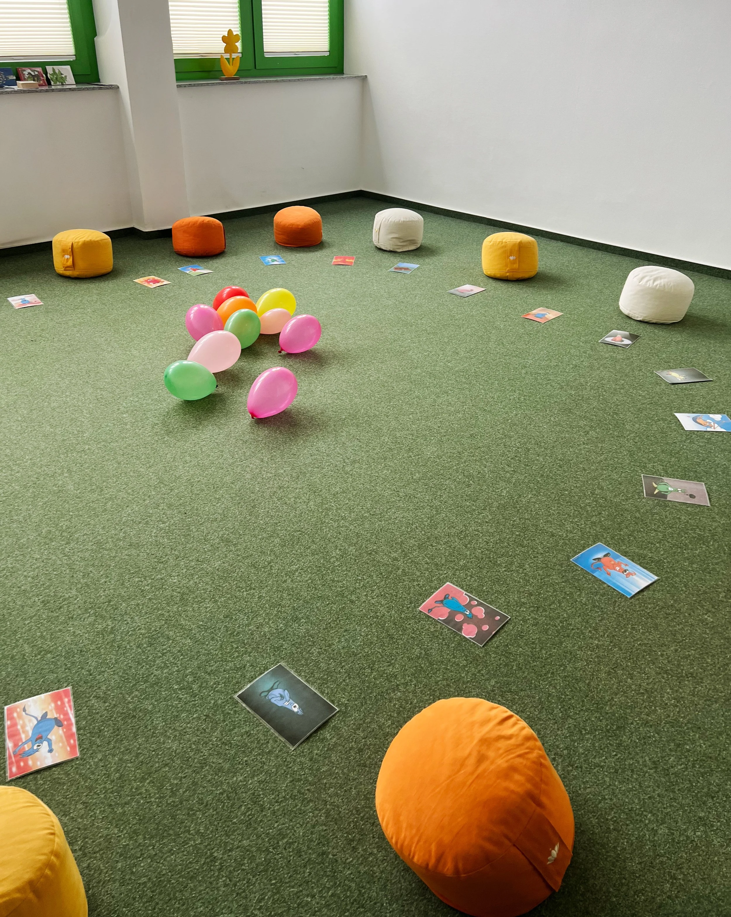 Ein Spielzimmer mit bunten Sitzsäcken, Luftballons in der Mitte und Bildern auf dem Boden, vermutlich für eine Kinderveranstaltung oder einen Spielbereich.