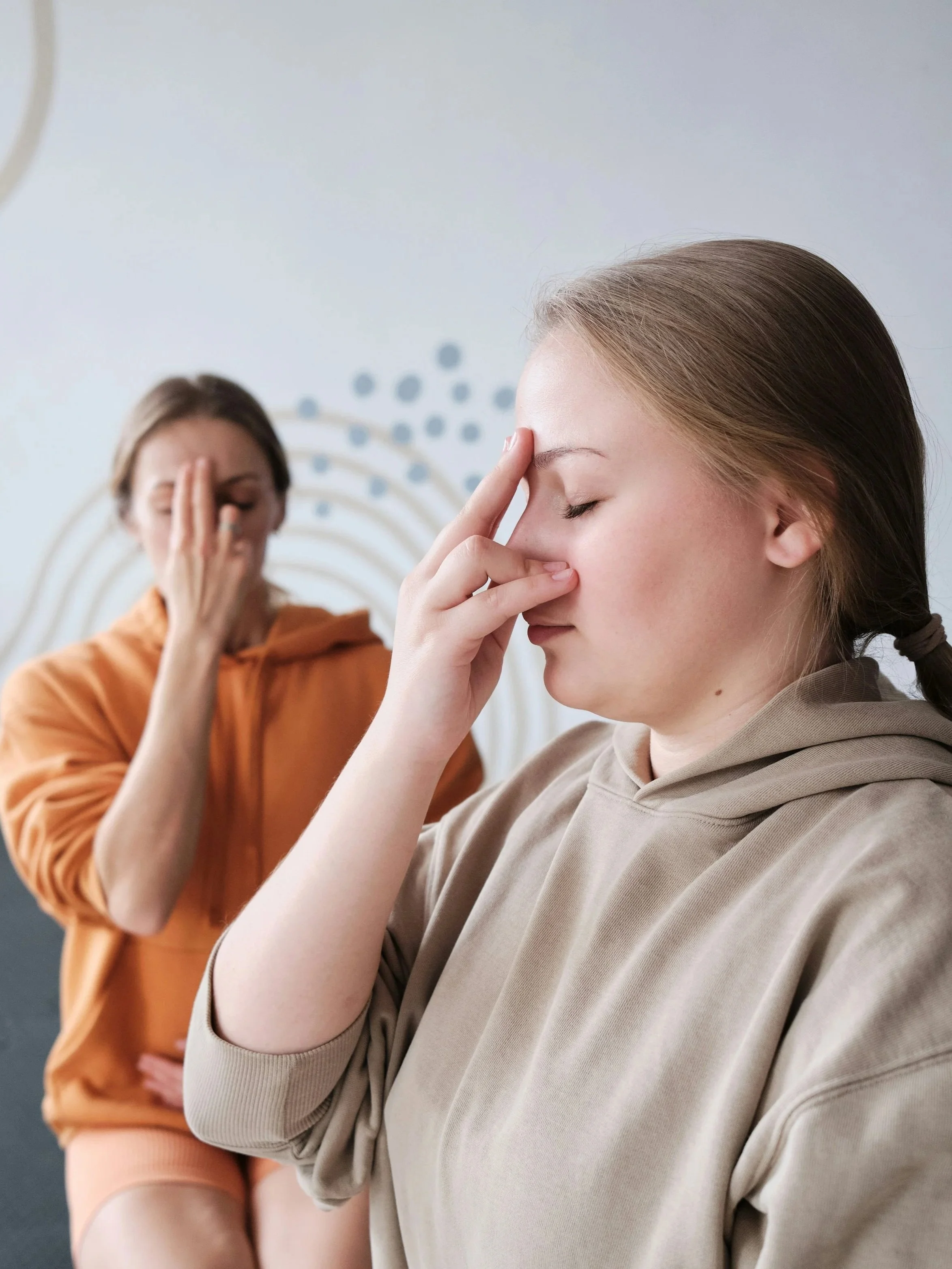 Zwei Menschen machen eine Atemübung oder Meditation, mit einer Hand auf der Stirn und der Nasenbrücke, die Augen geschlossen.
