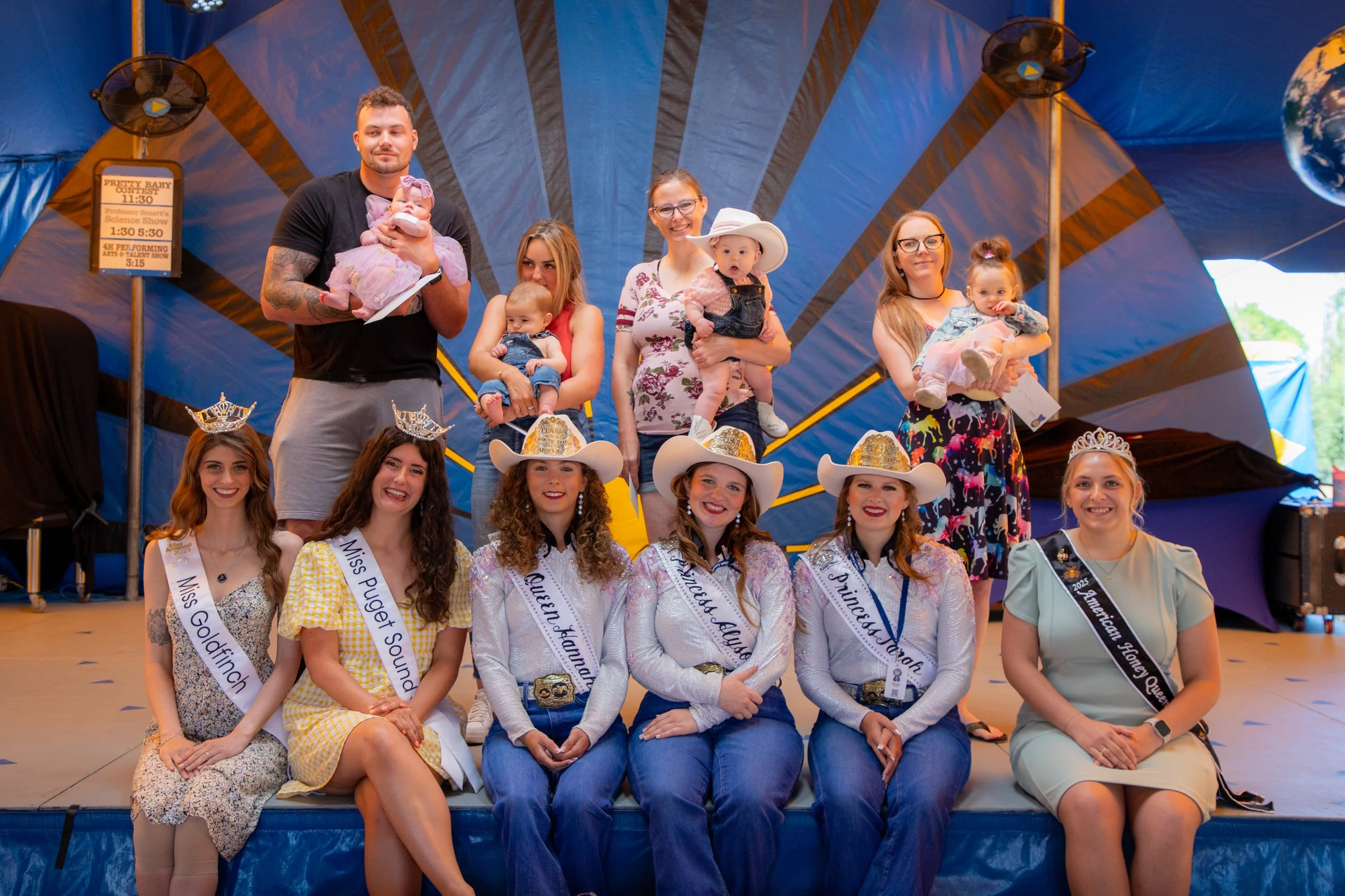 The winners of the 2025 Clark County Fair Pretty Baby Contest and the judges from the contest standing in front of a stage and smiling