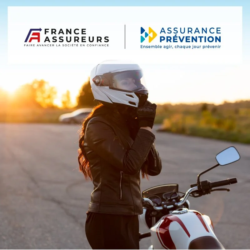 Une femme en équipement de moto, casque blanc, tenant son gant, avec une moto blanche et rouge, au coucher du soleil.