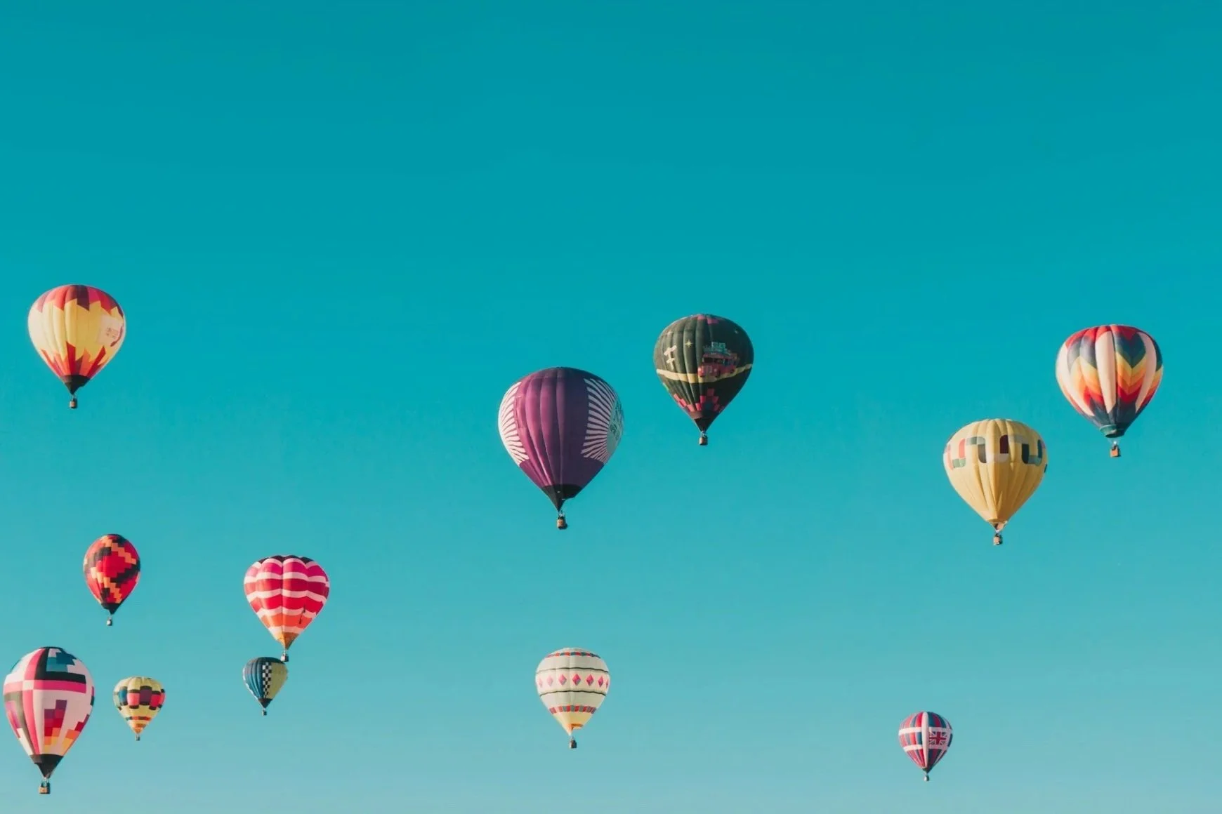 Plusieurs montgolfières colorées flottent dans un ciel clair et sans nuages.