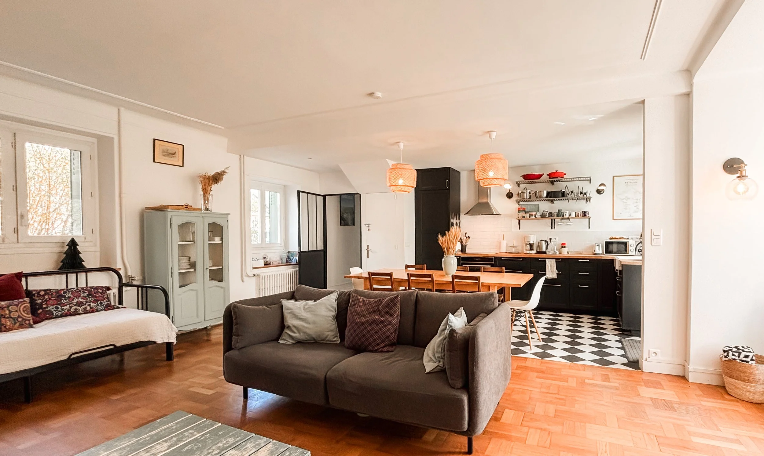 Intérieur d'un appartement avec un salon et une cuisine ouverts, meubles en bois, lampes suspendues en osier, velux, et décor cosy.