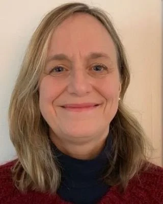 Close-up of a smiling woman with blonde hair, wearing a dark top and a red sweater.