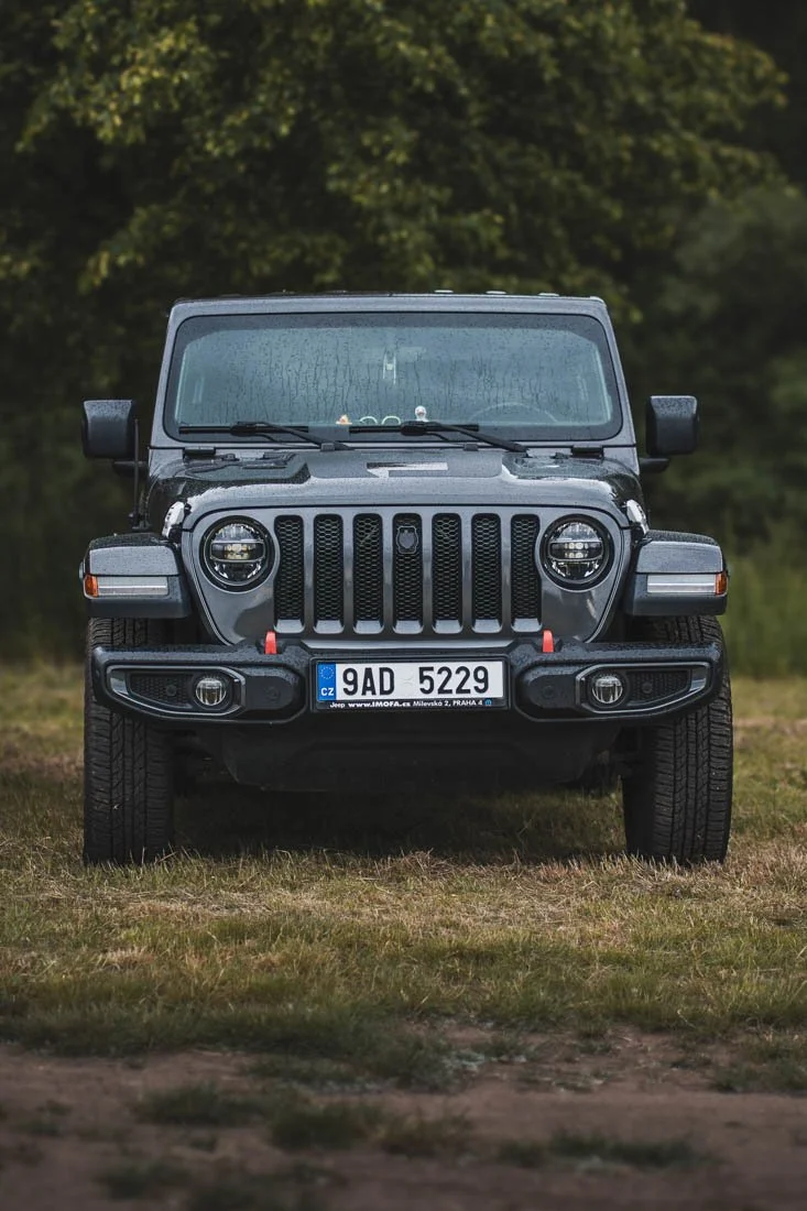 Front view of a gray Jeep Wrangler parked on grass with a background of green trees.