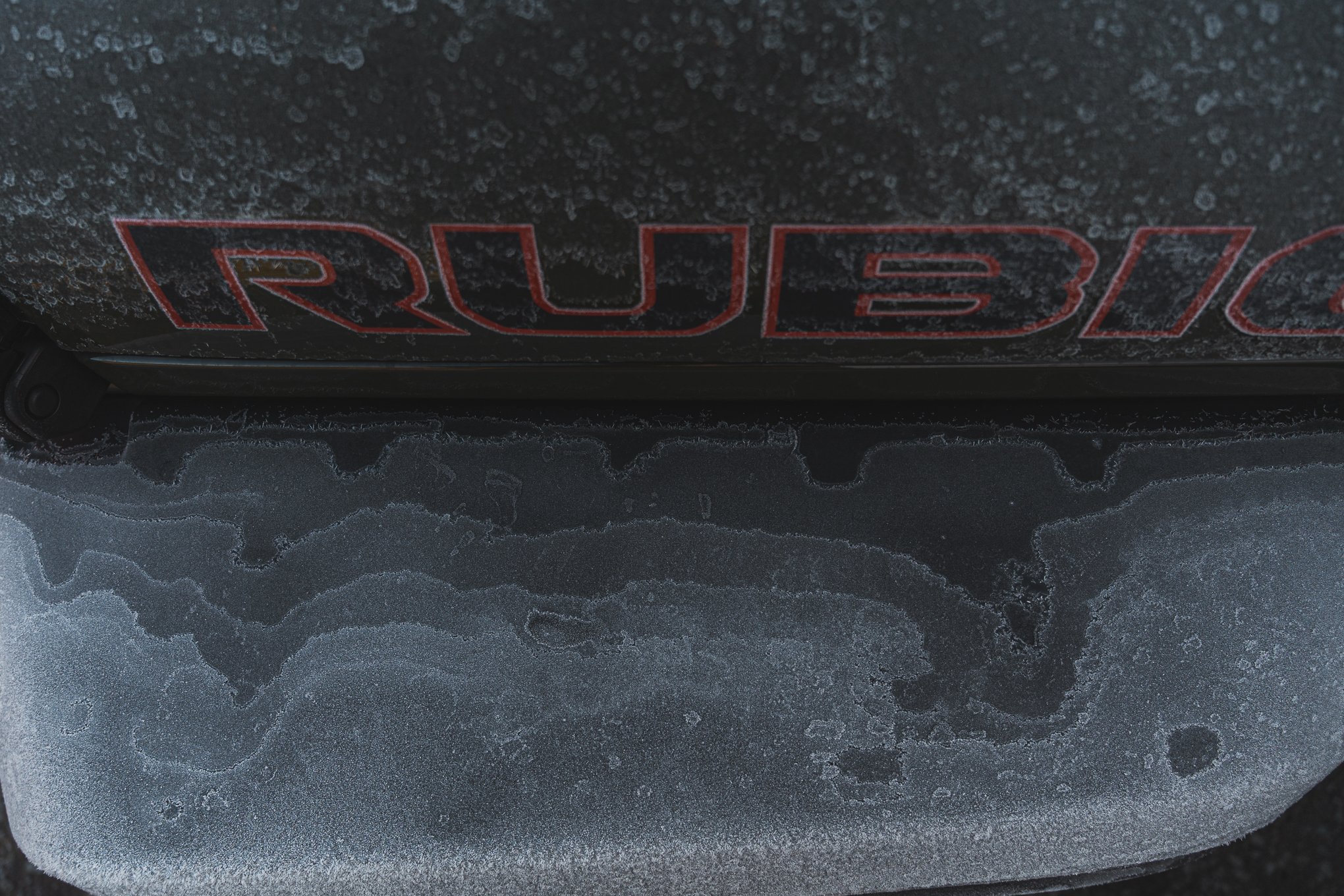 Close-up of a car tire with frost and ice buildup, with the top part showing a partially visible red and black logo or text.