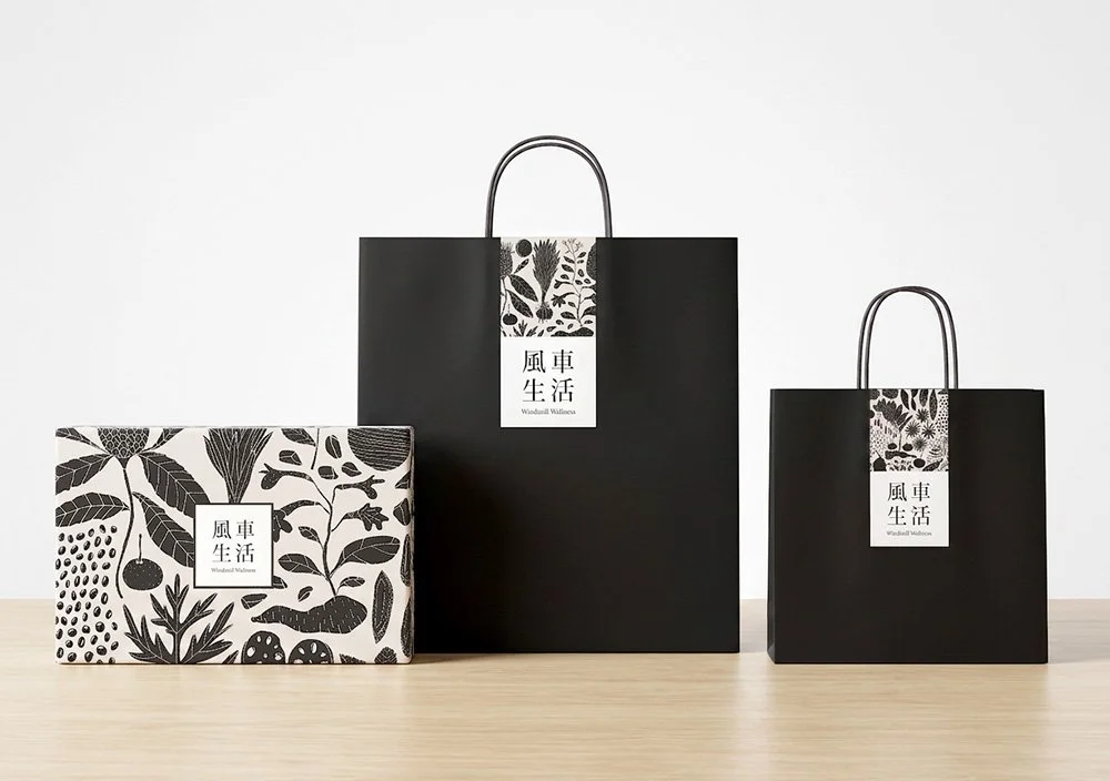 Three black and white paper shopping bags with floral and fruit designs, placed on a light-colored surface against a white background.
