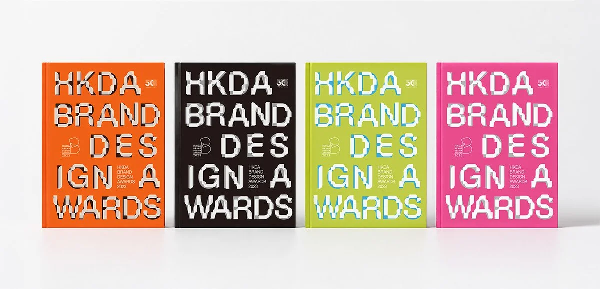 Four colorful books titled "HKDA Brand Design Awards 2023," with each book in orange, black, green, and pink covers, arranged side by side on a white surface.