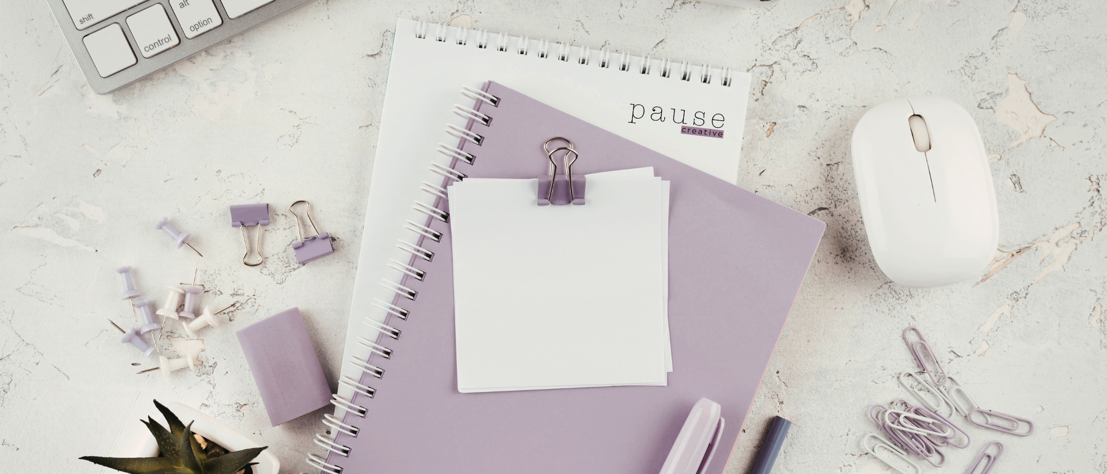 Flat lay of office or planner supplies including purple binders, white notepad with paperclip, white wireless mouse, assorted push pins and paper clips, and a small potted succulent plant on a light textured surface.