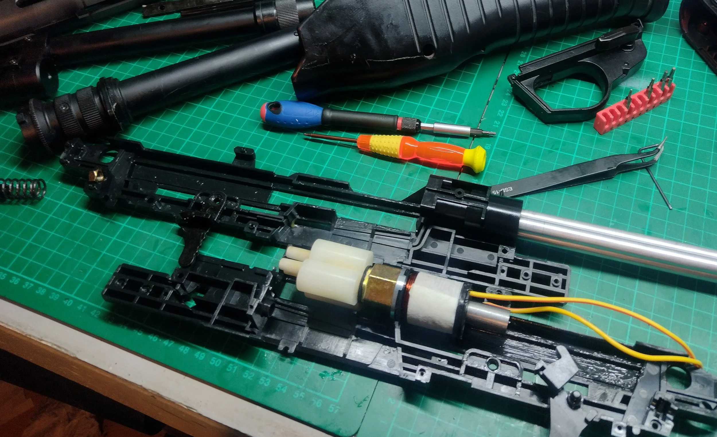 Disassembled airsoft gun internal parts and tools laid out on a green cutting mat.