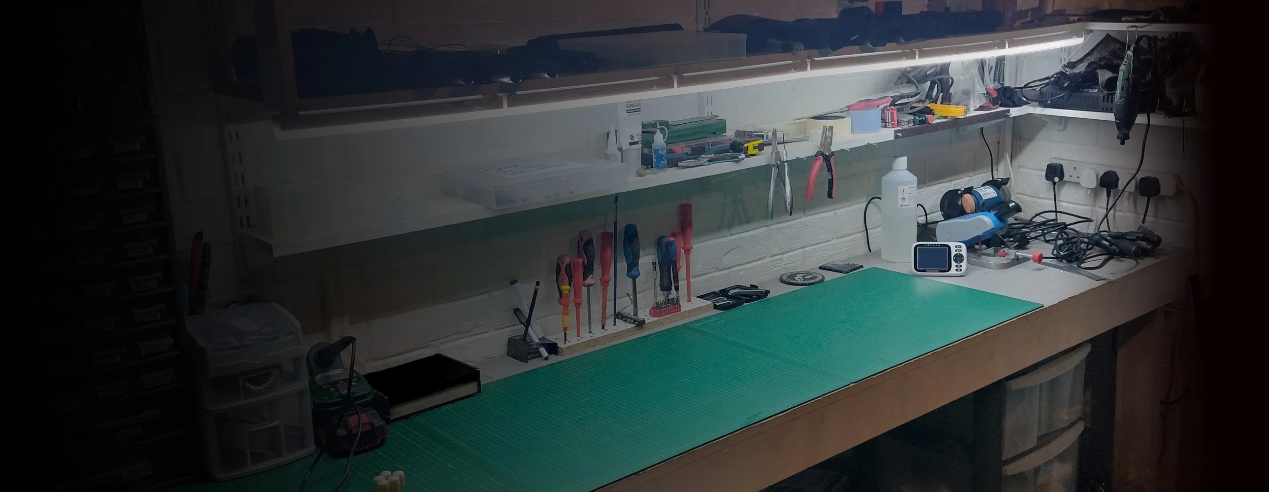 Airsoft workbench with various tools, a green cutting mat, and organized power strips in a workshop or maker space.