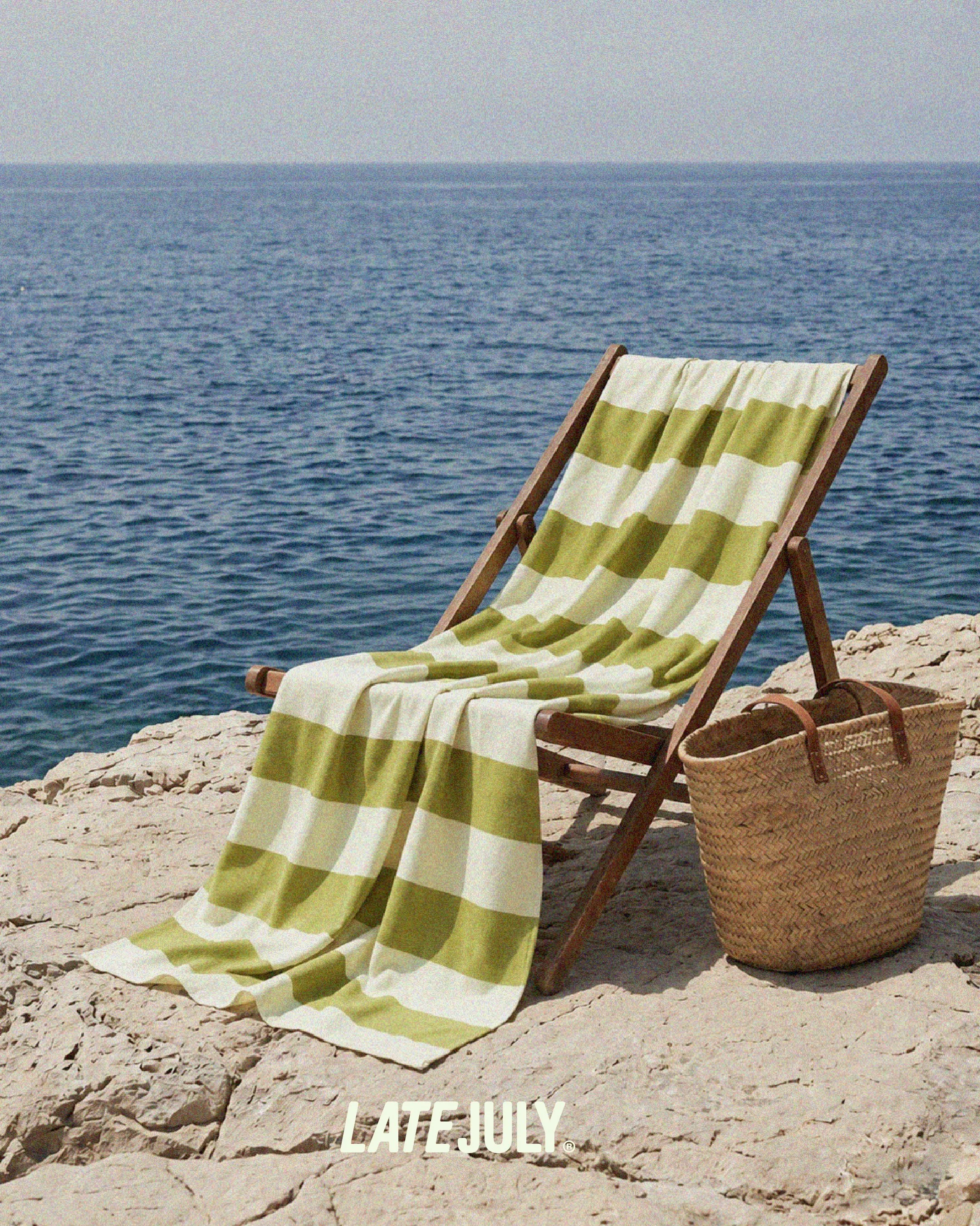 En strandstol ved en klippe. På strandstolen er et grønt og hvid stribet håndklæder, der matcher Late July's visuelle identitet og brand univers