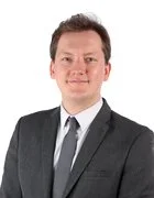 Photo of Headteacher in a dark suit and tie, smiling against a plain light background.