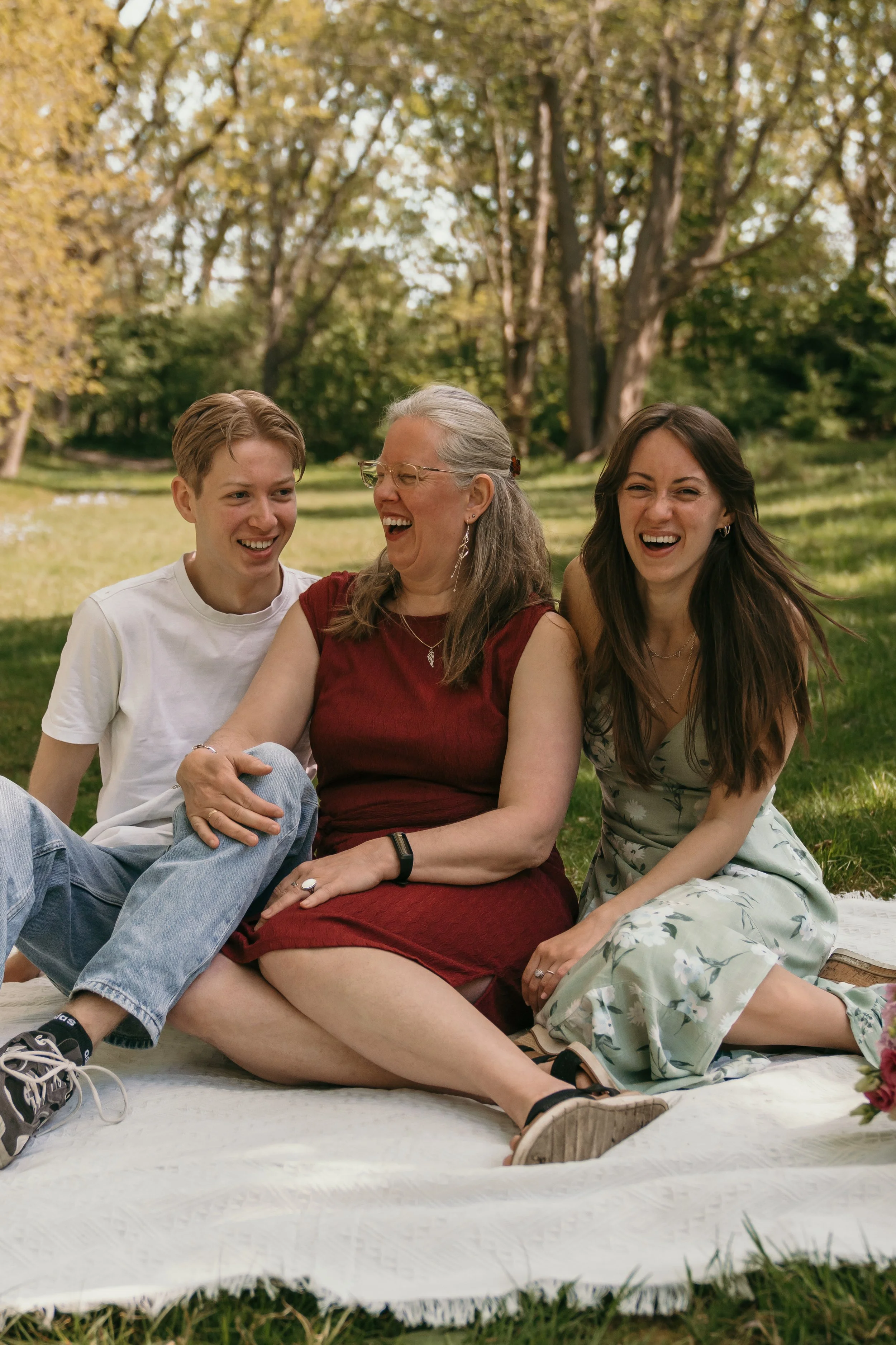 Gezin lacht samen op een grasveld in een bos, zittend op een picknickkleed.