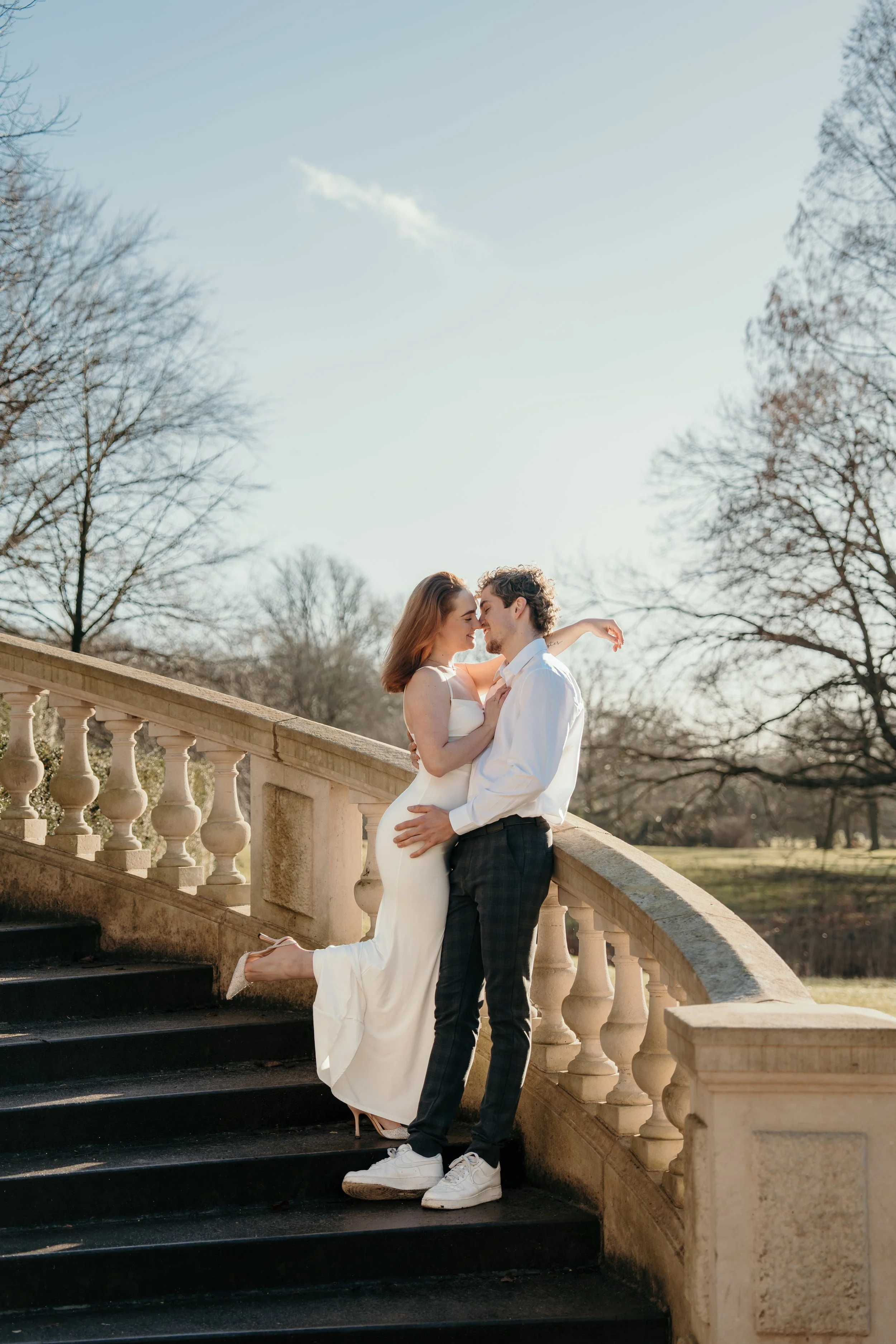 Een bruidspaar danst romantisch op een stenen trap buiten, met een park en bomen op de achtergrond met zonnig weer tijdens een bruidsreportage van Rosa Lynn Signer.