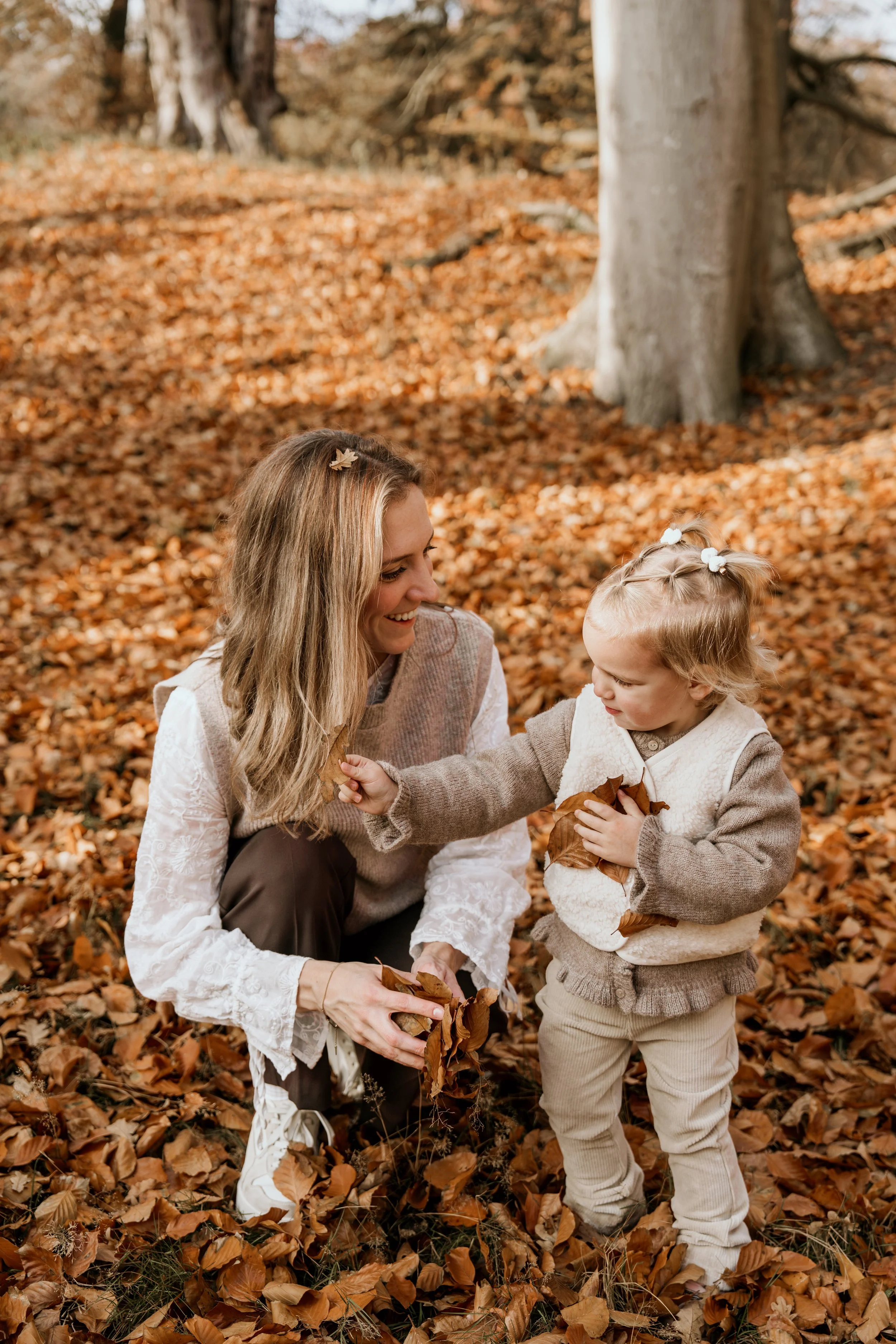 Moeder en dochter spelen met herfst bladeren in een bos tijdens een motherhoodshoot van Rosa Lynn Signer.