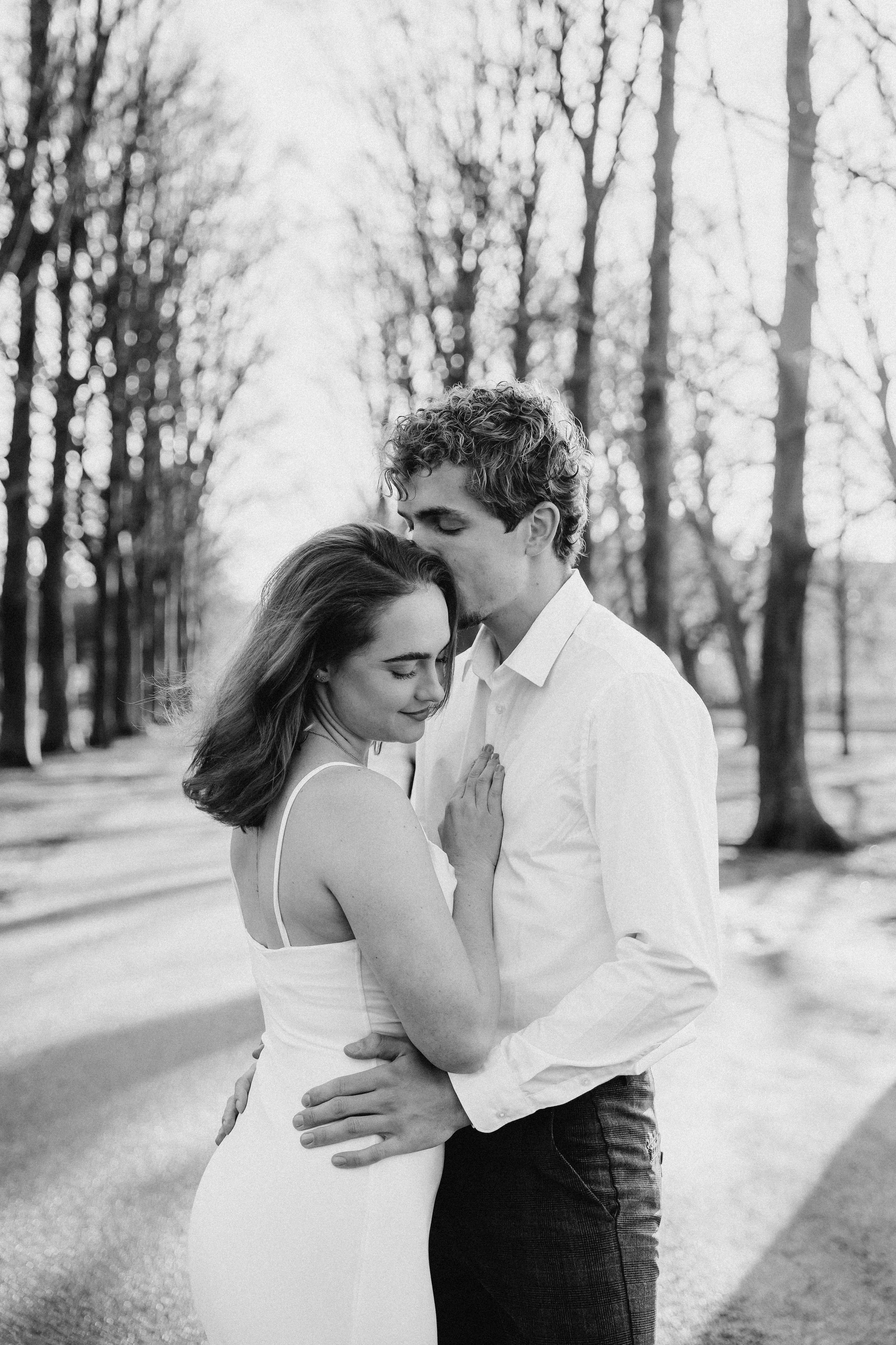 Een zwart-wit foto van een verliefd bruidspaar dat in een park staat, de bruidegom kust de bruid op haar voorhoofd terwijl zij met gesloten ogen glimlacht tijdens een bruidsreportage van Rosa Lynn Signer.