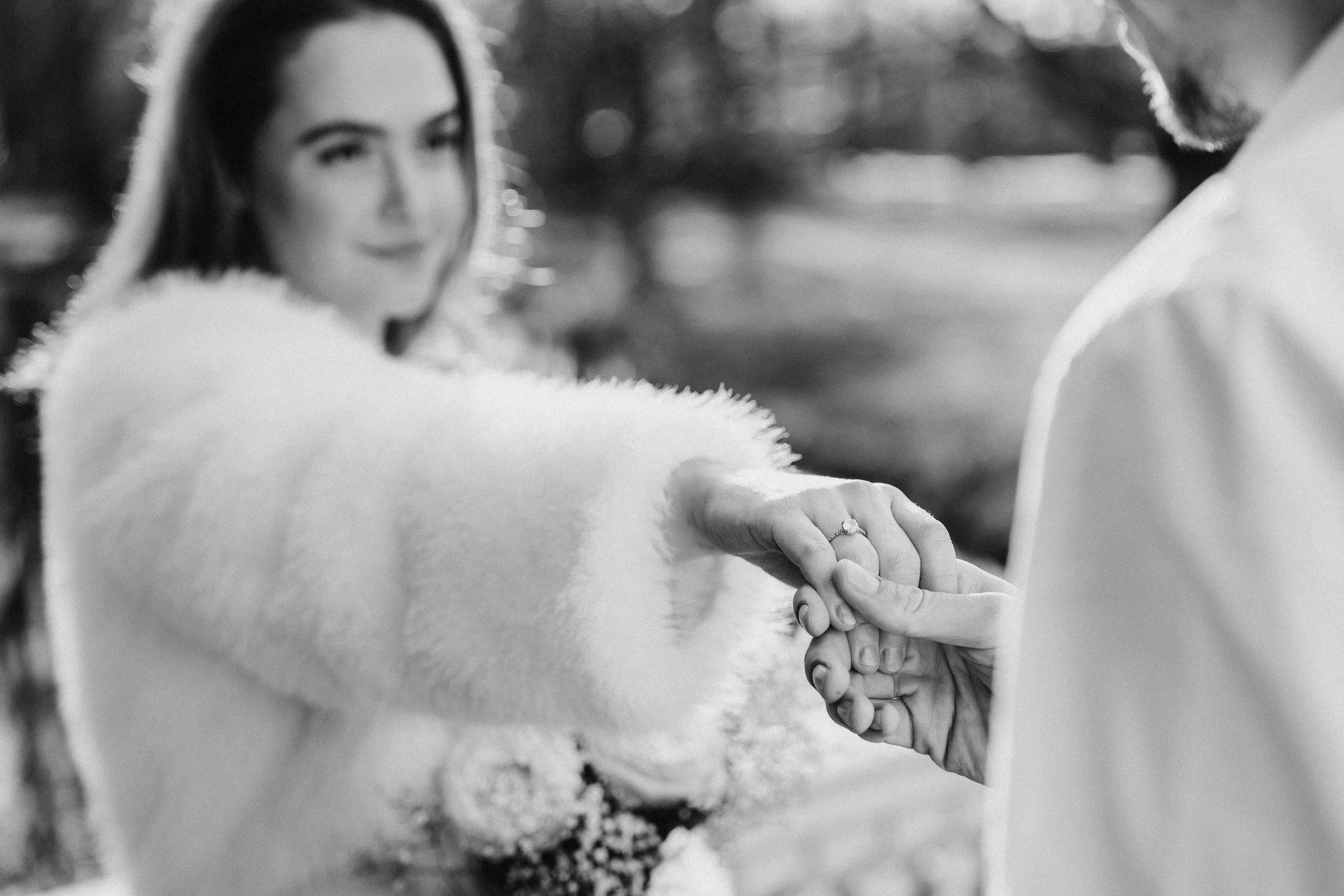Een bruid en bruidegom houden elkaars handen vast tijdens hun huwelijk, met de focus op hun handen en de huwelijksring op de vinger van de bruid, in een zwart-wit foto tijdens een bruidsreportage van Rosa Lynn Signer.