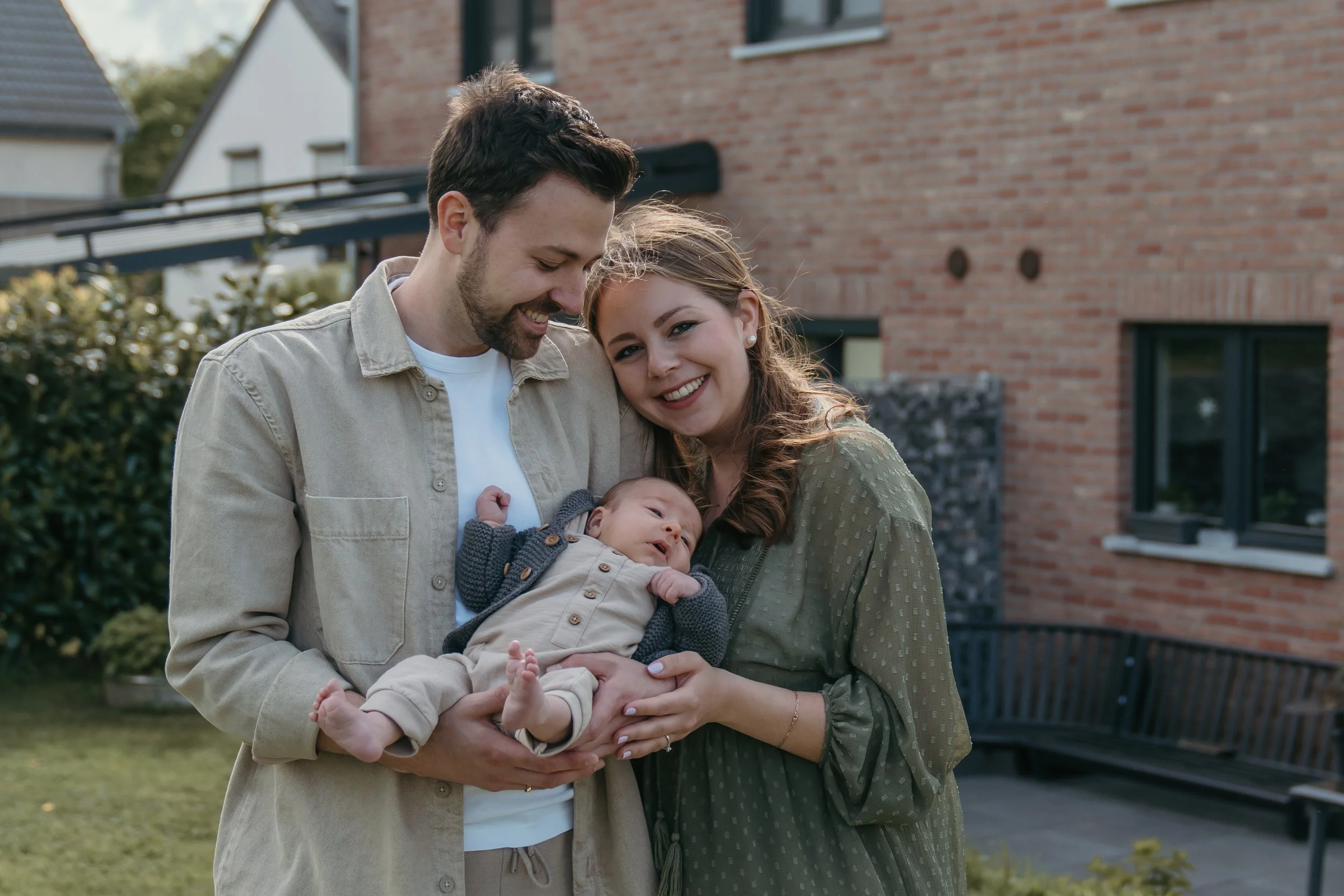 Nieuw ouders houden samen trots hun new born vast baby in een tuin tijdens een new life shoot van Rosa Lynn Signer. 