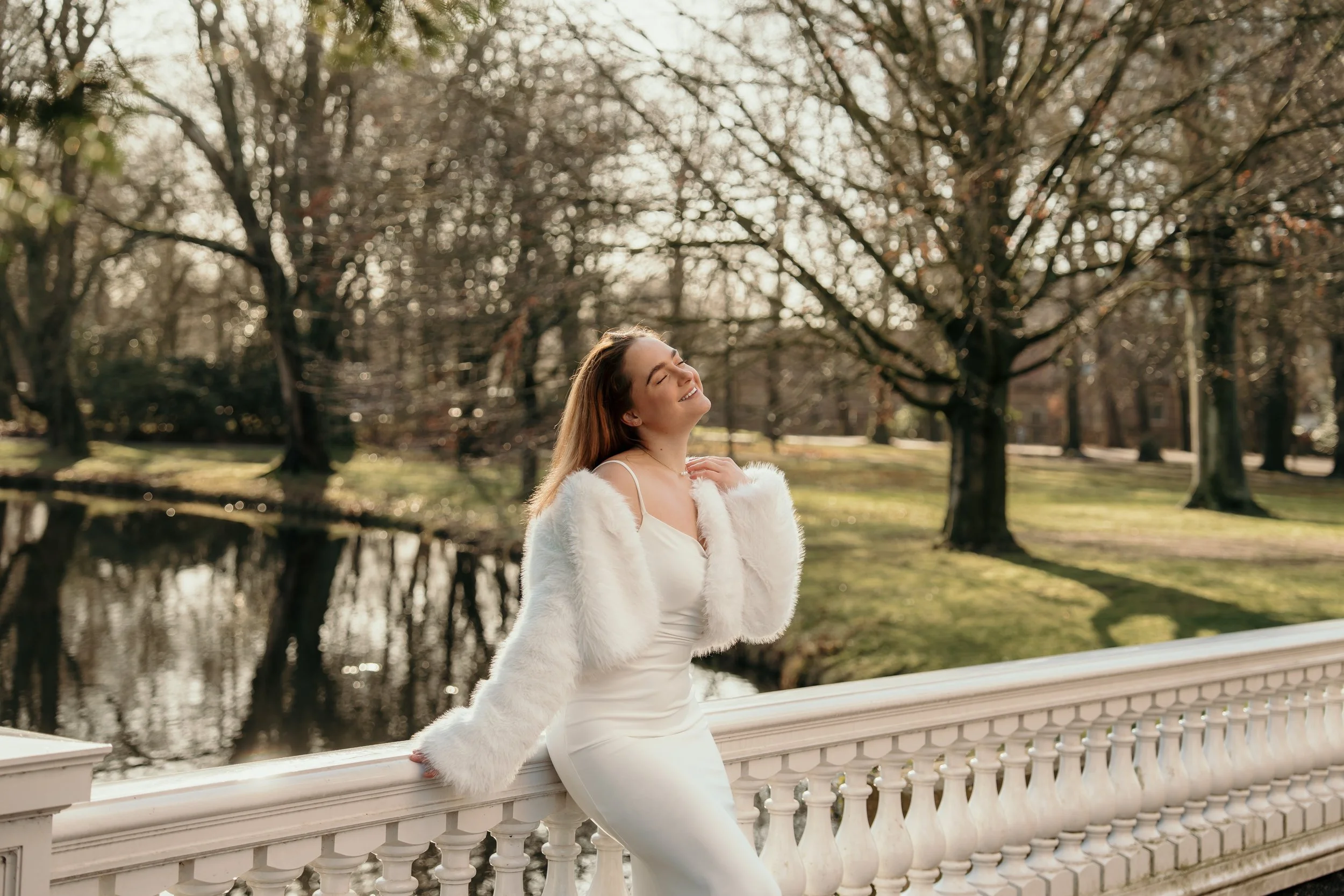 Een bruid in haar trouwjurk en bontjas leunt tegen een witte balustrade op een landgoed tijdens een bruidsreportage van Rosa Lynn Signer.
