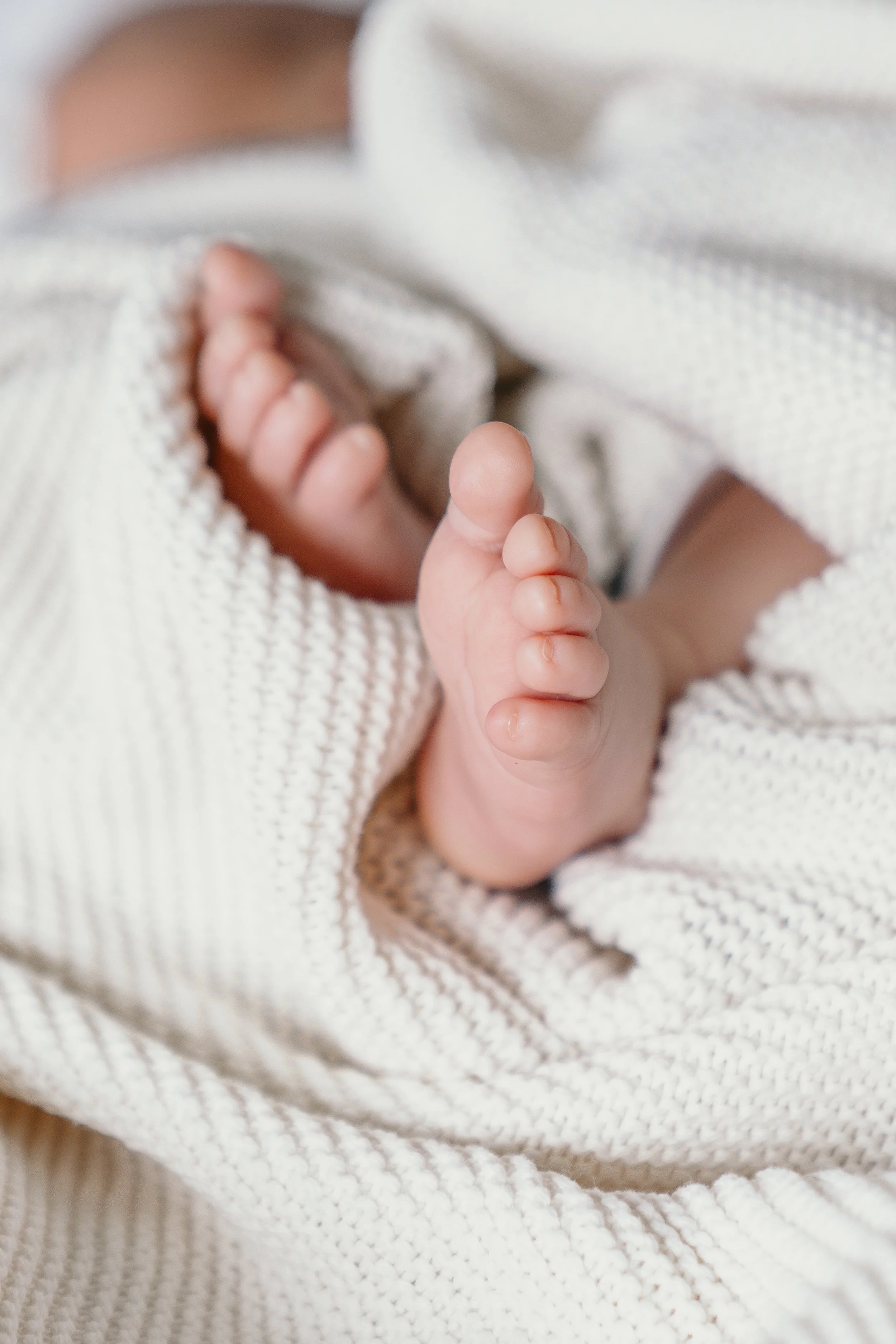 Close-up van een babyvoet in een witte, geribbelde doek, zichtbaar vanaf de tenen tot halverwege de voet. Tijdens een new born shoot van Rosa Lynn Signer. 