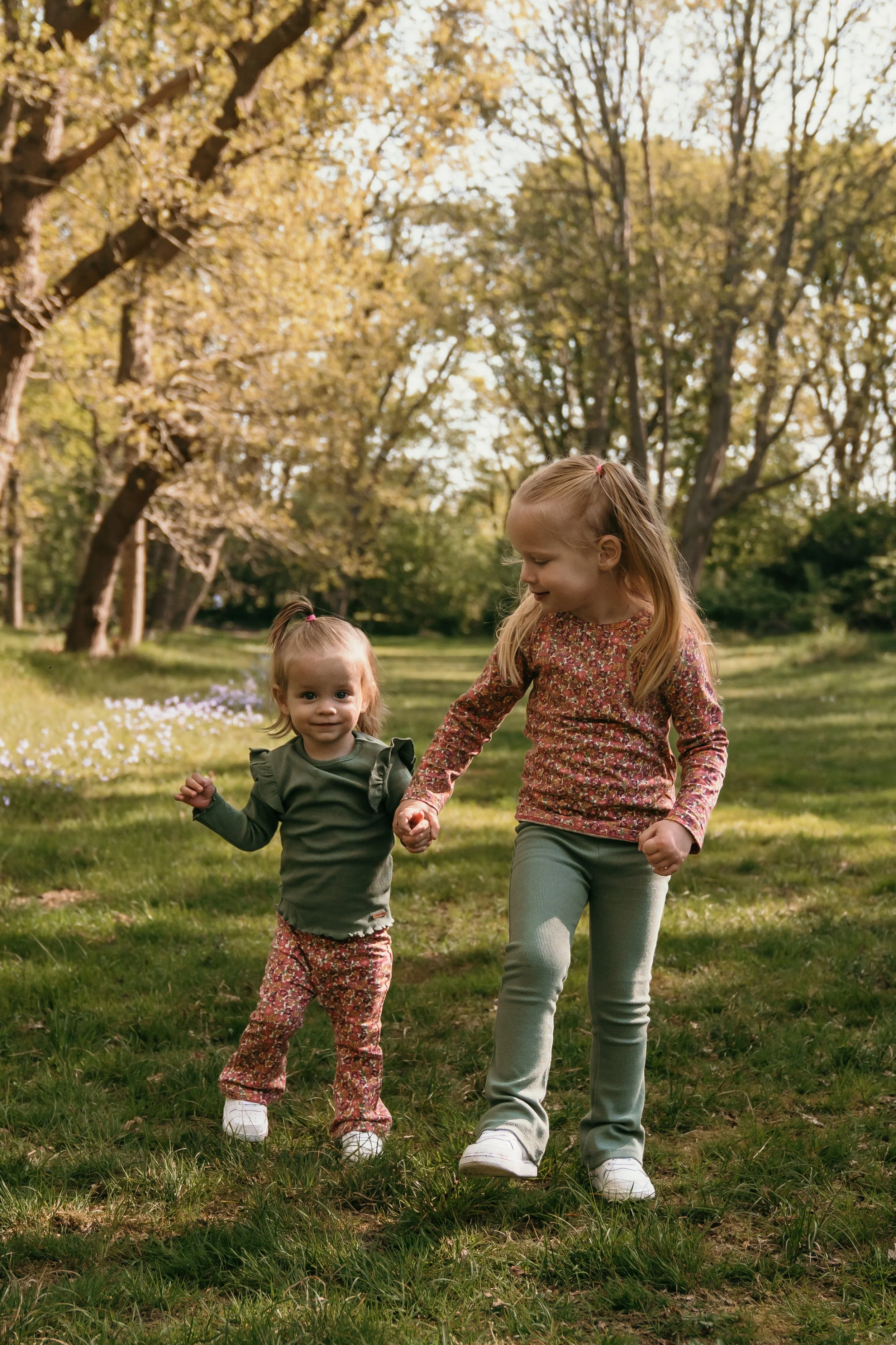 Twee jonge meisjes wandelen hand in hand in een bos tijdens een gezinsshoot van Rosa Lynn Signer.