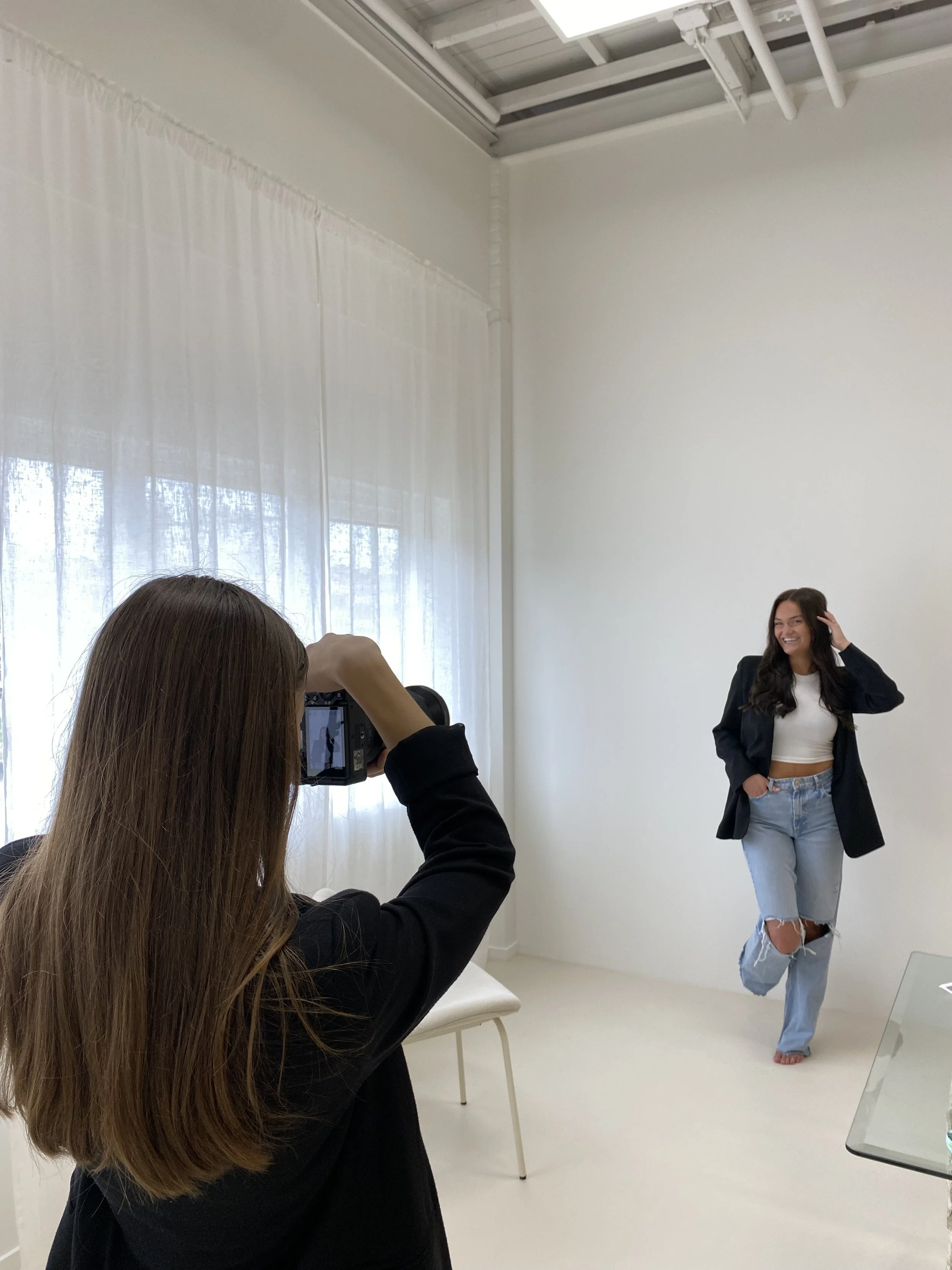 Rosa Lynn Signer maakt een foto's in een daglicht studio,  van een model die poseert met een hand in haar zak en een andere hand in haar haar.