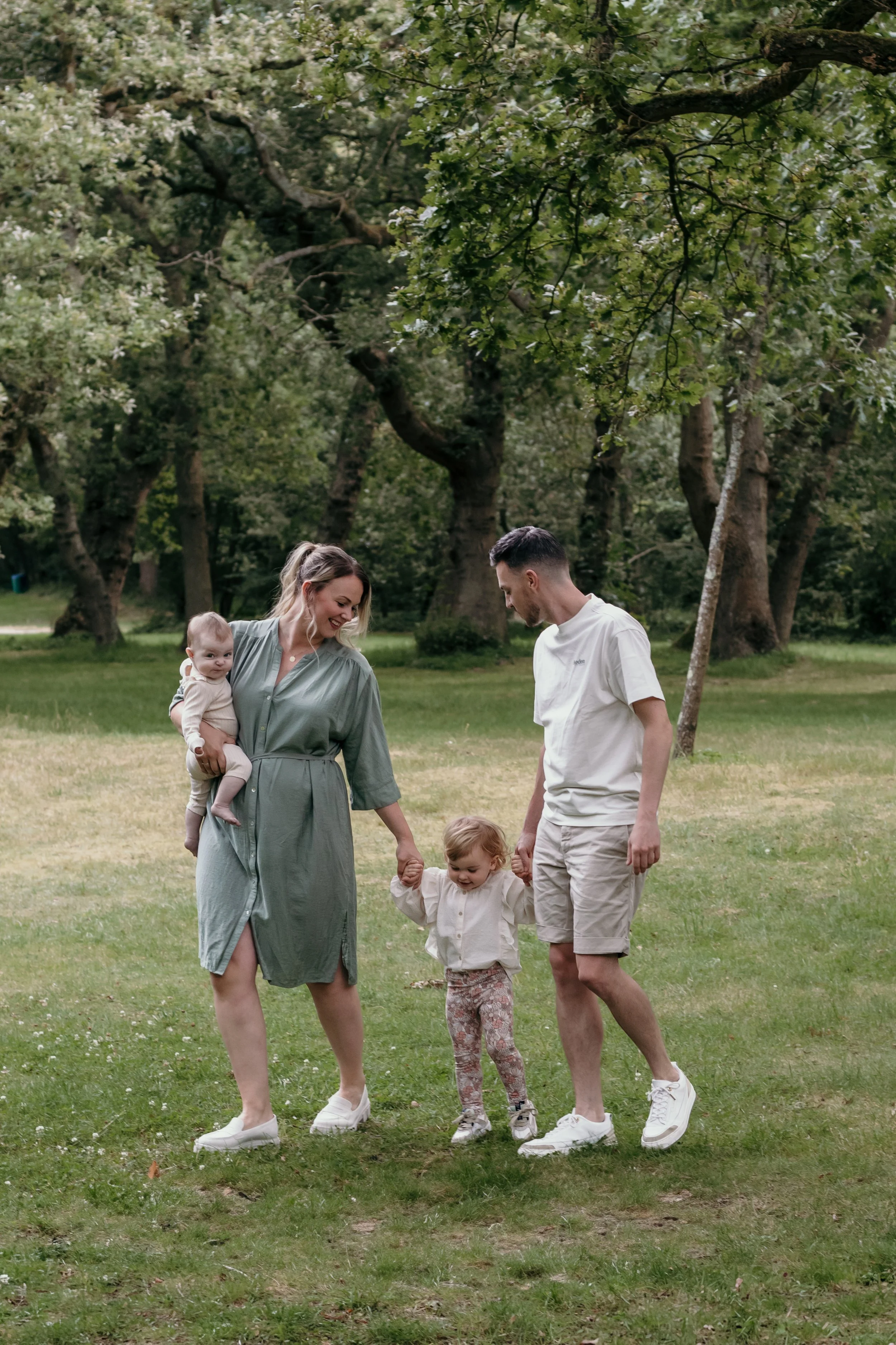 Een gezin van vier wandelen samen in een bos, lachend en hand in hand. Familieshoot van Rosa Lynn Signer.