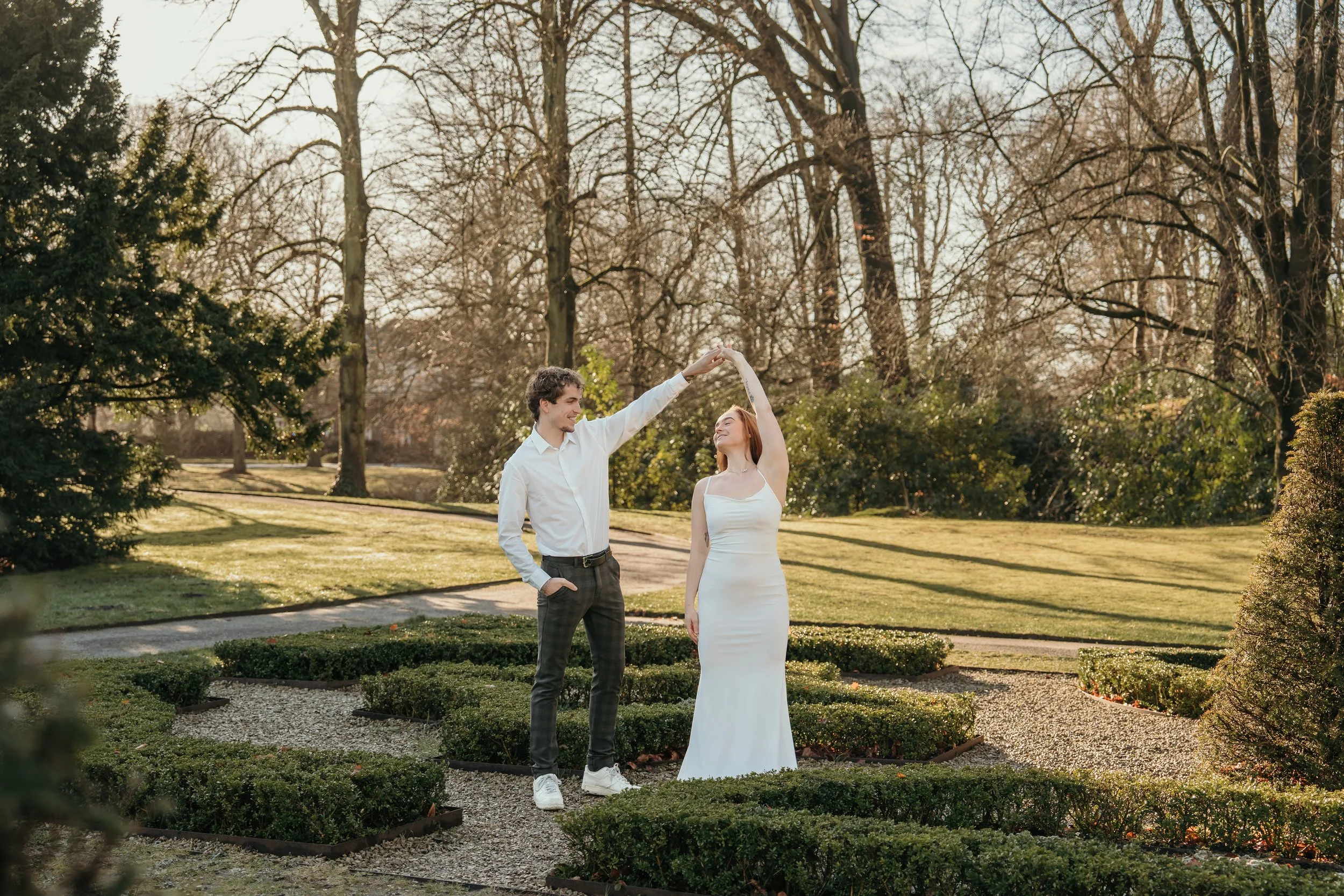 Een bruidspaar danst in een park op een zonnige dag, een man en een vrouw in een witte jurk, omringd door struiken en bomen tijdens een bruidsreportage van Rosa Lynn Signer.