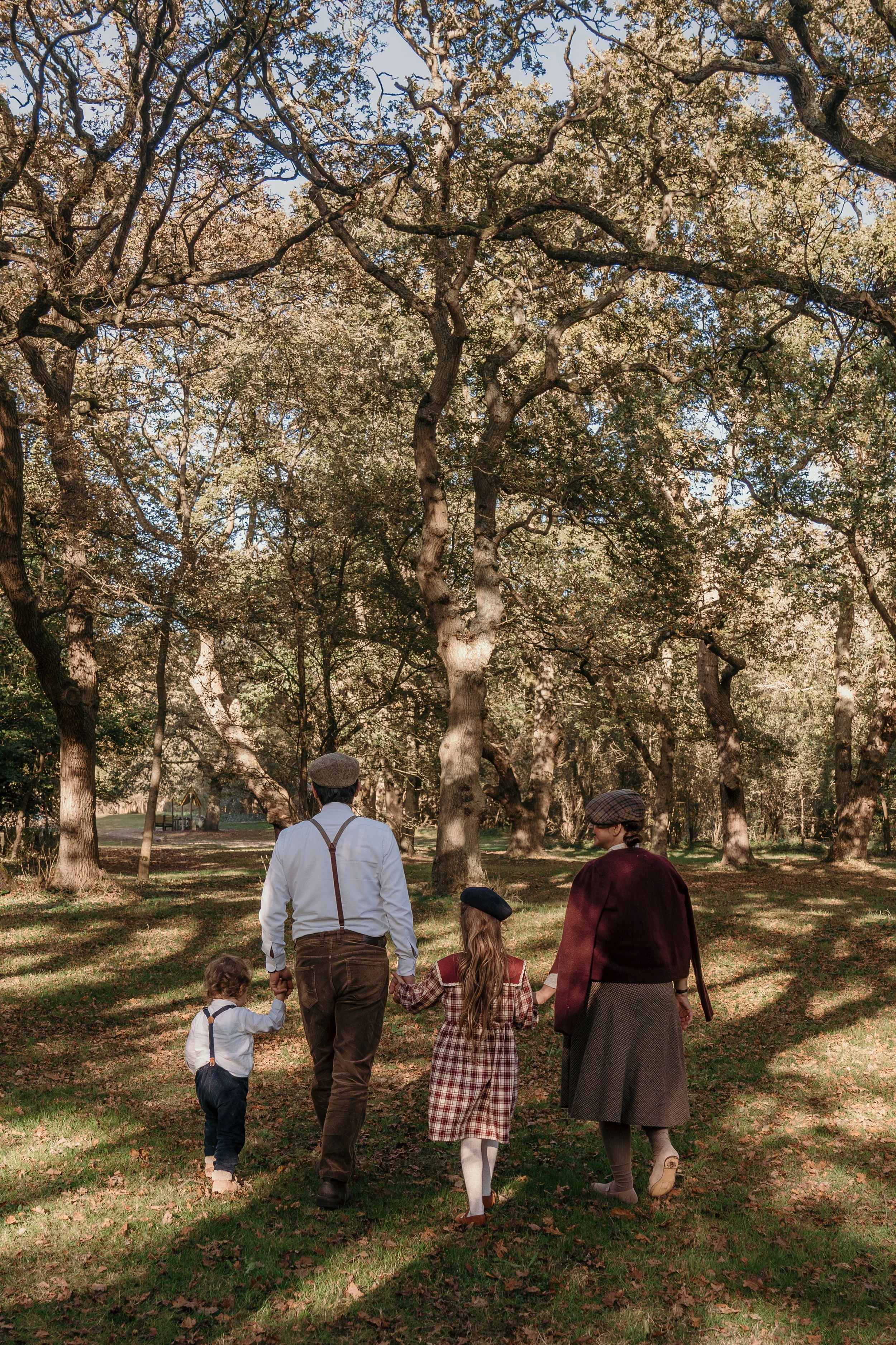 Een familie wandelend door een park met grote bomen, vermomd in vintage kleding, in de herfst tijdens een gezinsshoot van Rosa Lynn Signer.