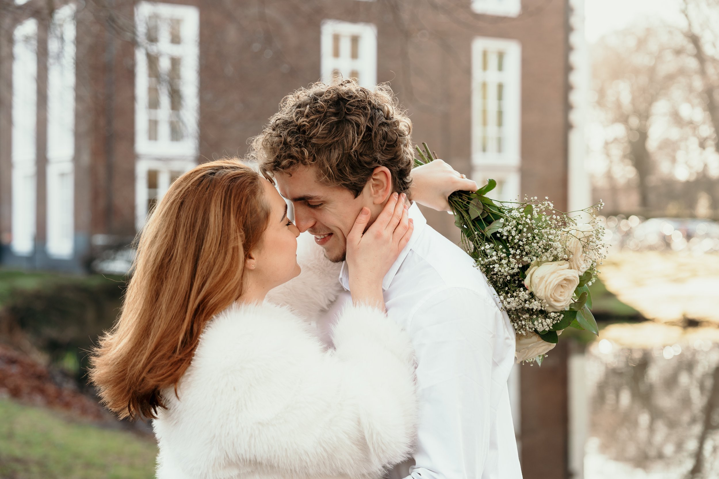 Een verliefd bruidspaar dat elkaar in de ogen kijkt, omringd door een romantische sfeer buiten, met een meisje dat een boeket bloemen vasthoudt tijdens een bruidsreportage van Rosa Lynn Signer.