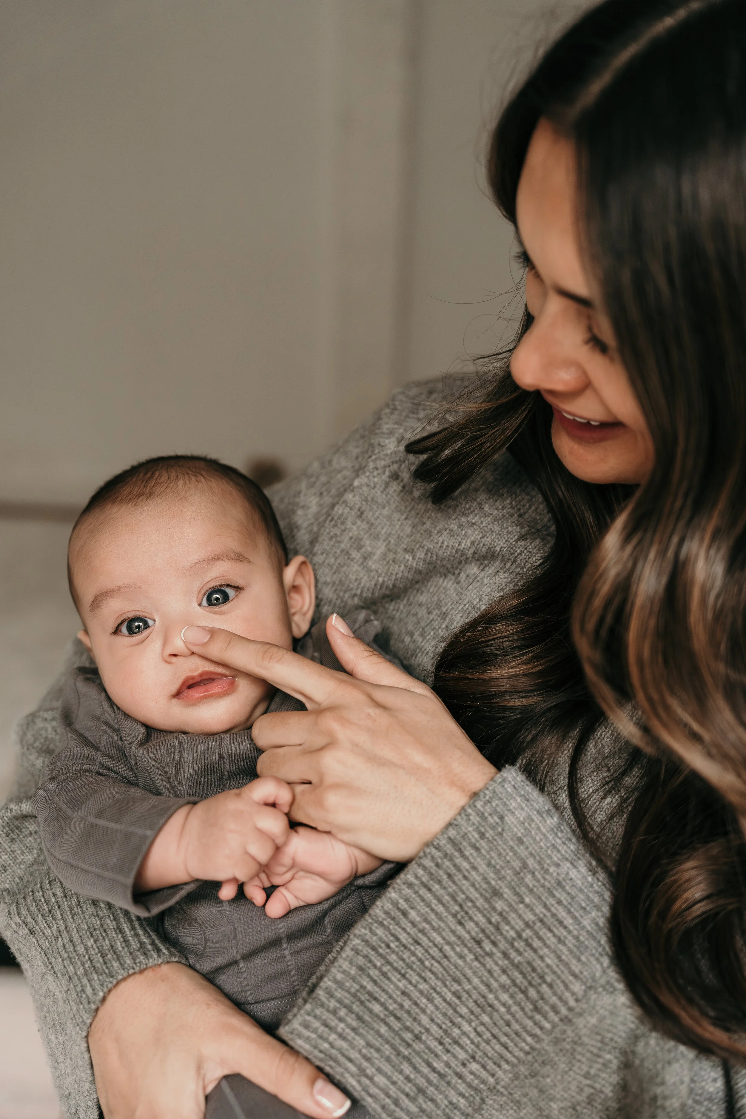 Een nieuwe moeder speelt met haar baby. Mama lacht en de new born kijkt verbaasd terwijl ze haar neusje omhoog houdt tijdens een new life shoot van Rosa Lynn Signer. 