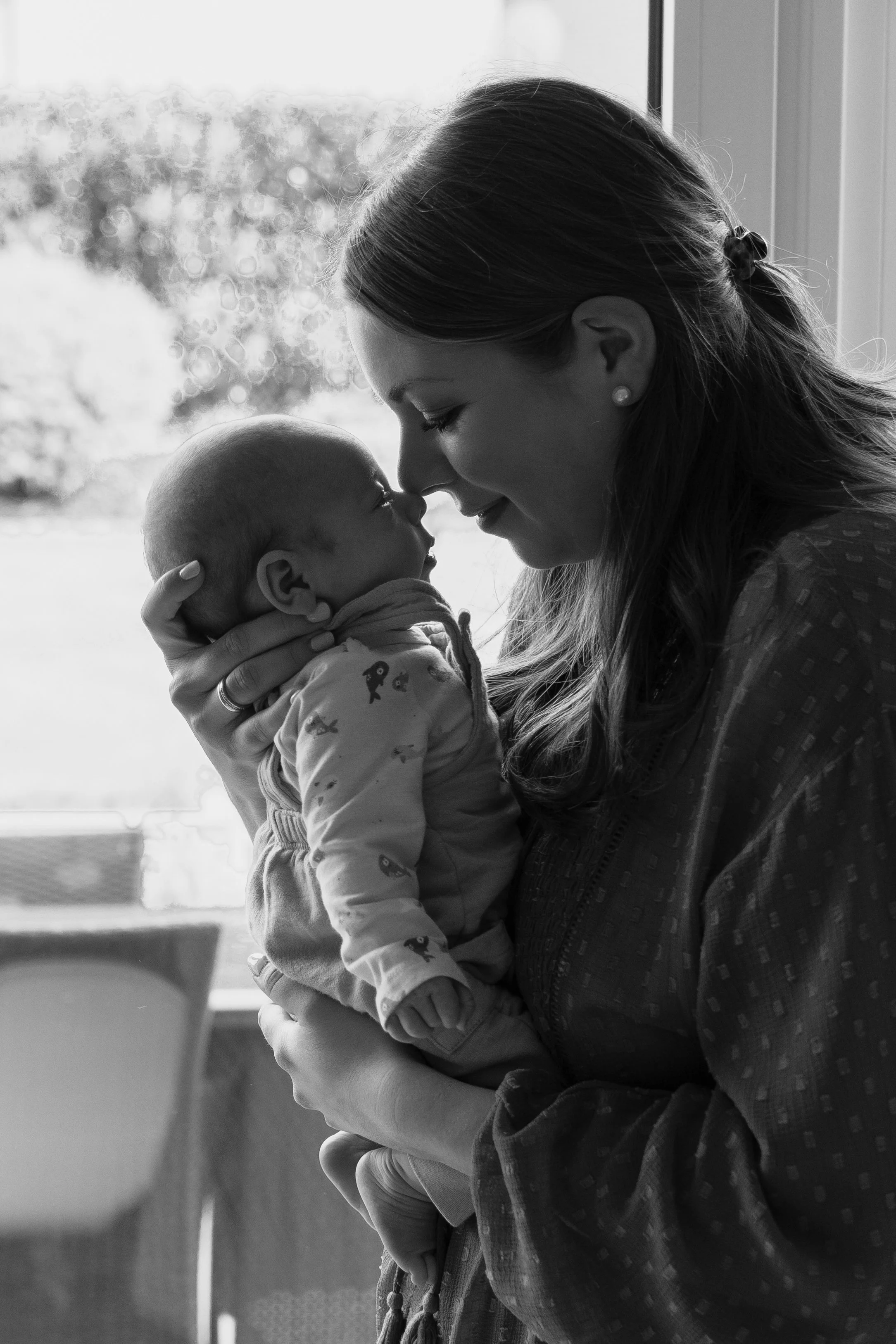 Moeder houdt haar baby bij zich en kijkt liefdevol naar haar new born tijdens een new life shoot van Rosa Lynn Signer. 