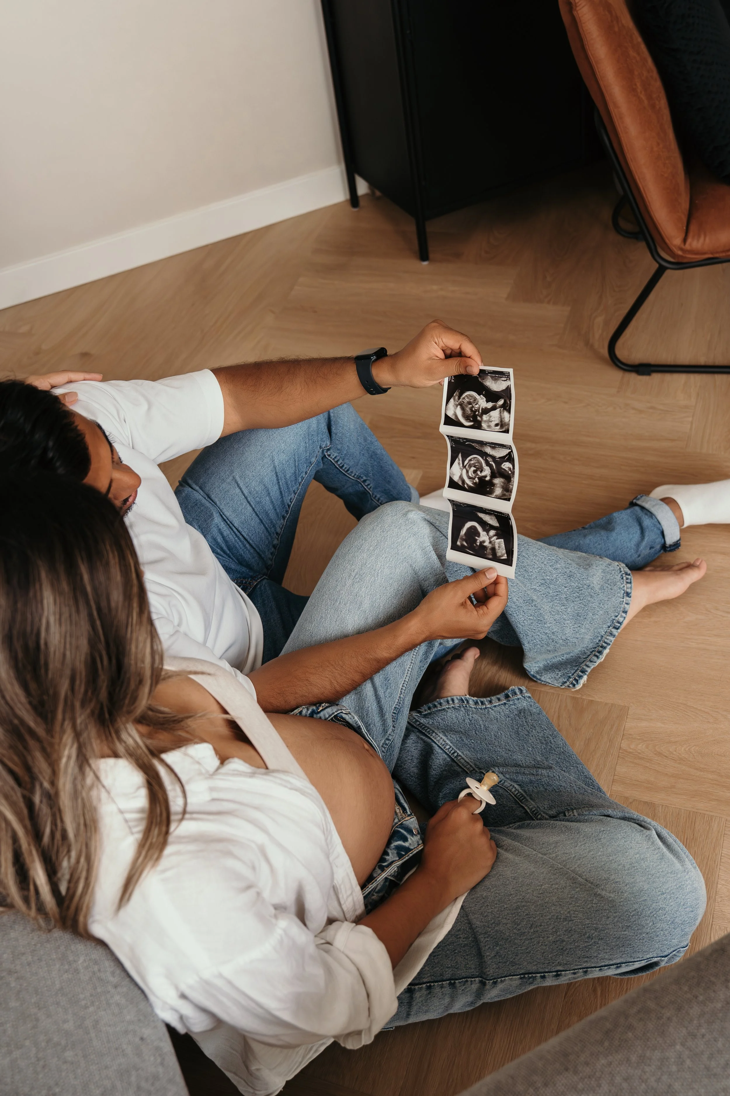 Een zwangere vrouw en haar partner bekijken samen een echo van de baby tijdens een zwangerschapsshoot van Rosa Lynn Signer.