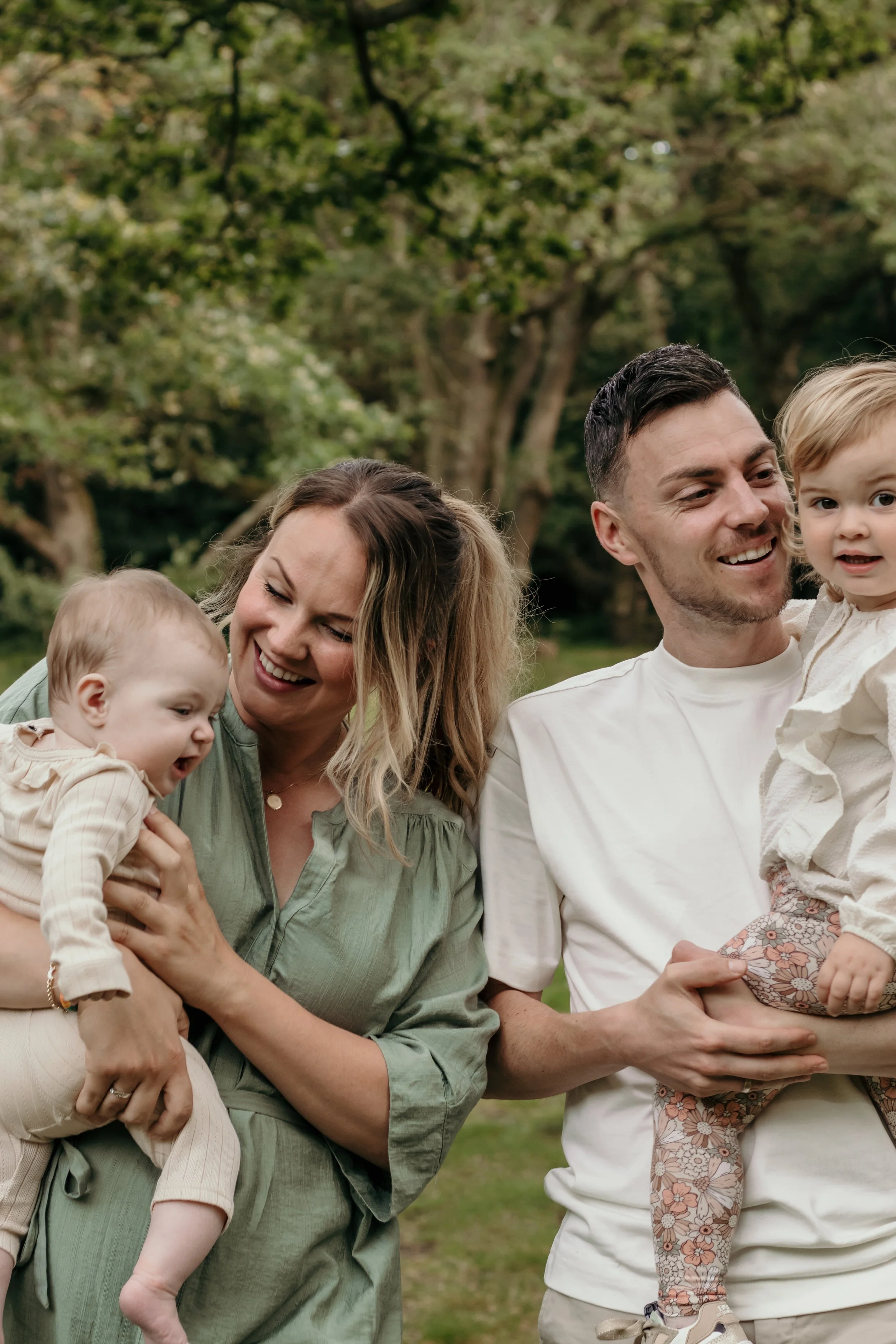 Een gezin van vier mensen geniet van een wandeling in een park, omgeven door groen en bomen tijdens een gezinsshoot van Rosa Lynn Signer.