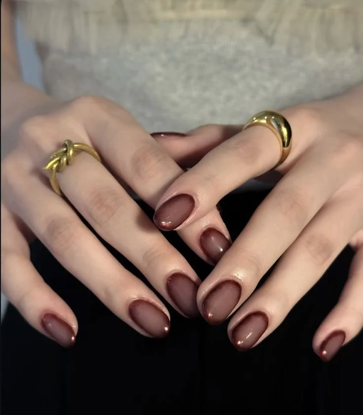 Close-up of a person's hands with manicured nails and gold rings on fingers, held together forming a heart shape.