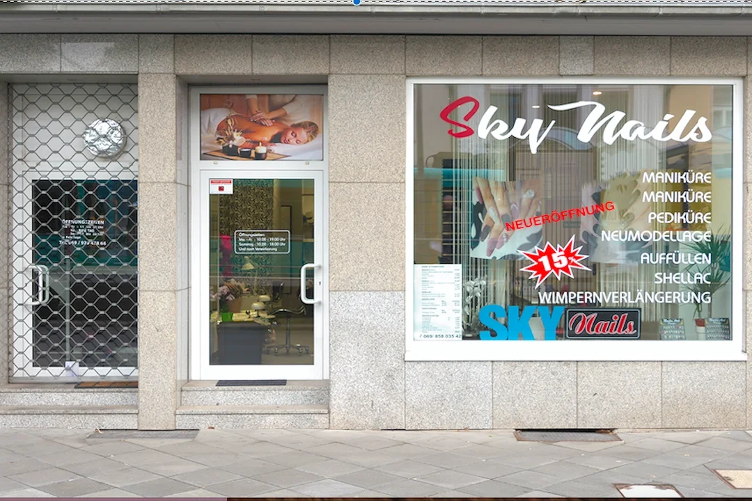Exterior view of a nail salon called 'Sky Nails' with signage listing services like manicures, pedicures, and nail enhancements, and a large window displaying a promotional poster.
