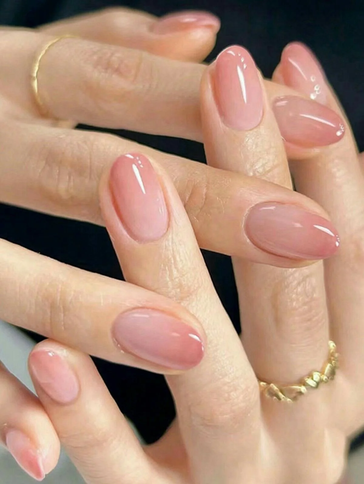 Close-up of well-manicured nails with natural pink glossy polish on fingers, some adorned with gold rings.