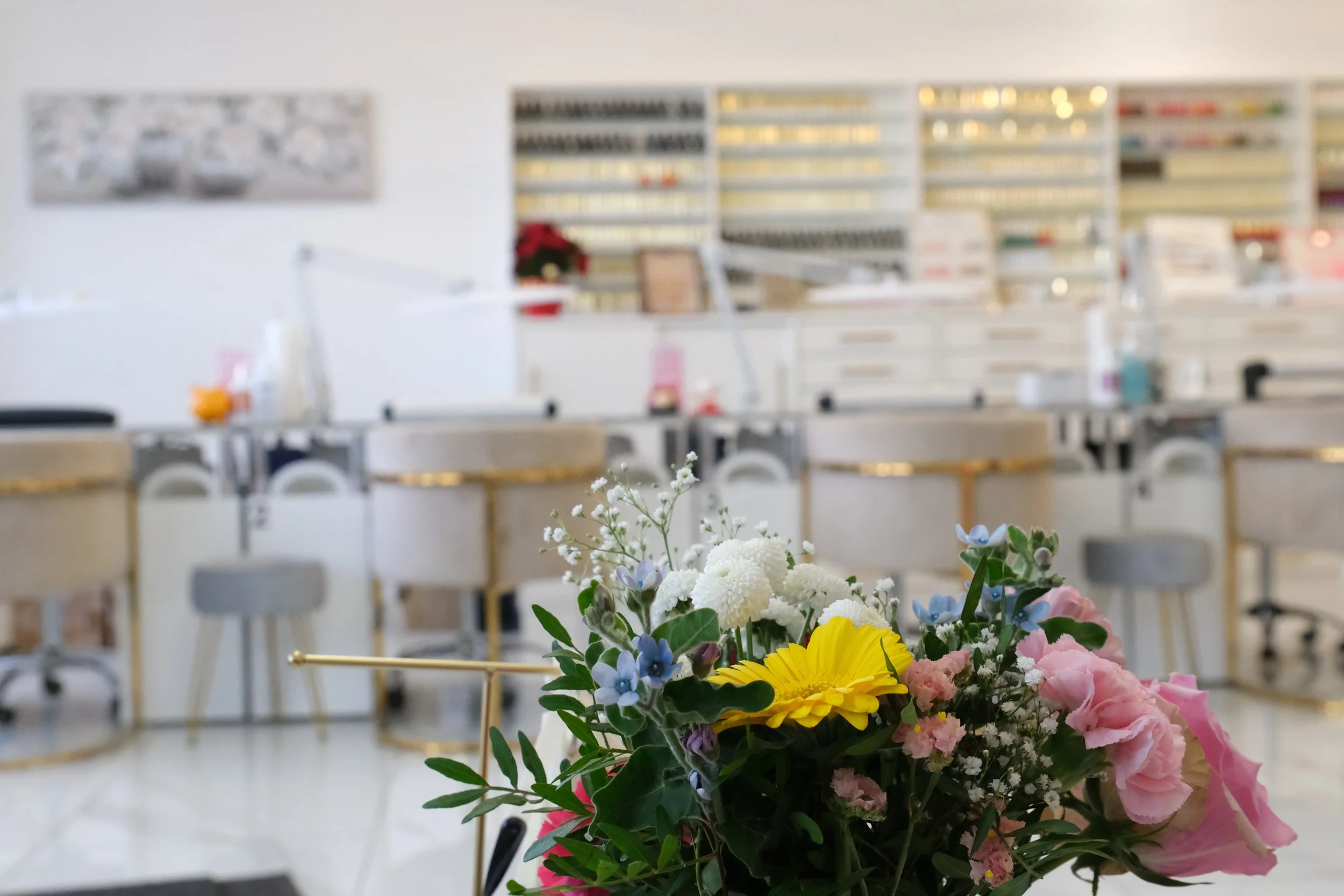 A bouquet of colorful flowers in the foreground with a blurred background of a pharmacy interior, featuring shelves stocked with medications and a white counter.