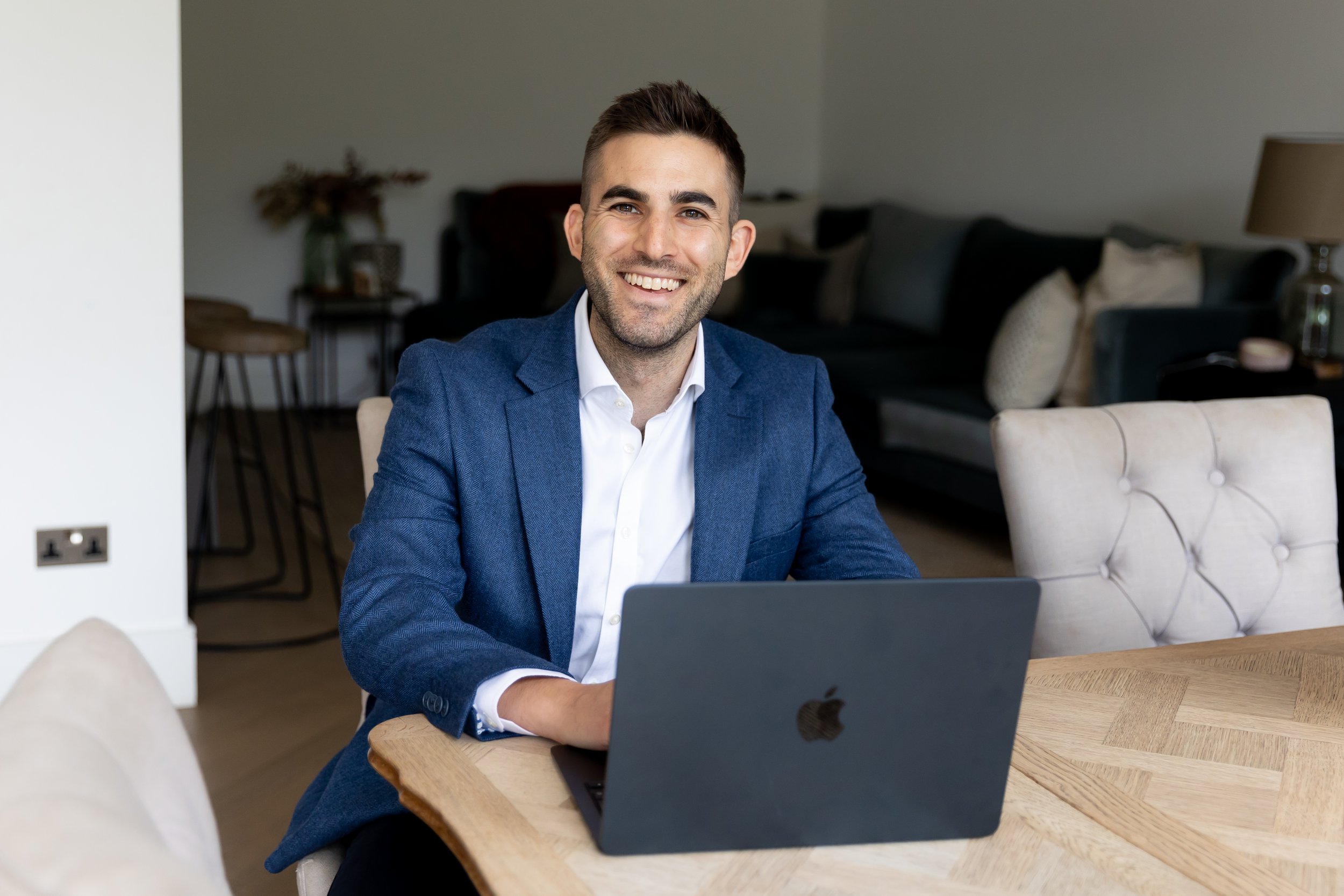 Dr Matt Slavin, Clinical Psychologist in a blue suit jacket sitting at a wooden table with a laptop in a living room.