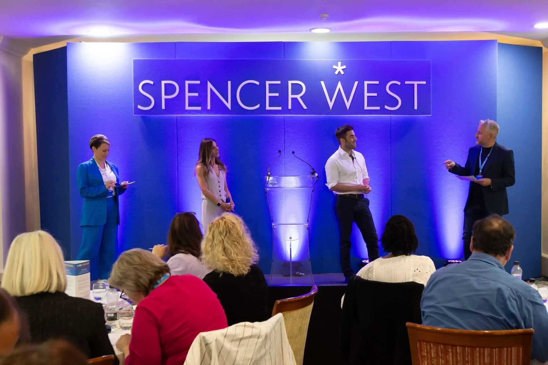 Panel discussion at a conference with four people on stage, two men and two women, including Dr Matt Slavin, Clinical Psychologist, in front of a blue wall with 'Spencer West' written on it, and an audience seated at tables.