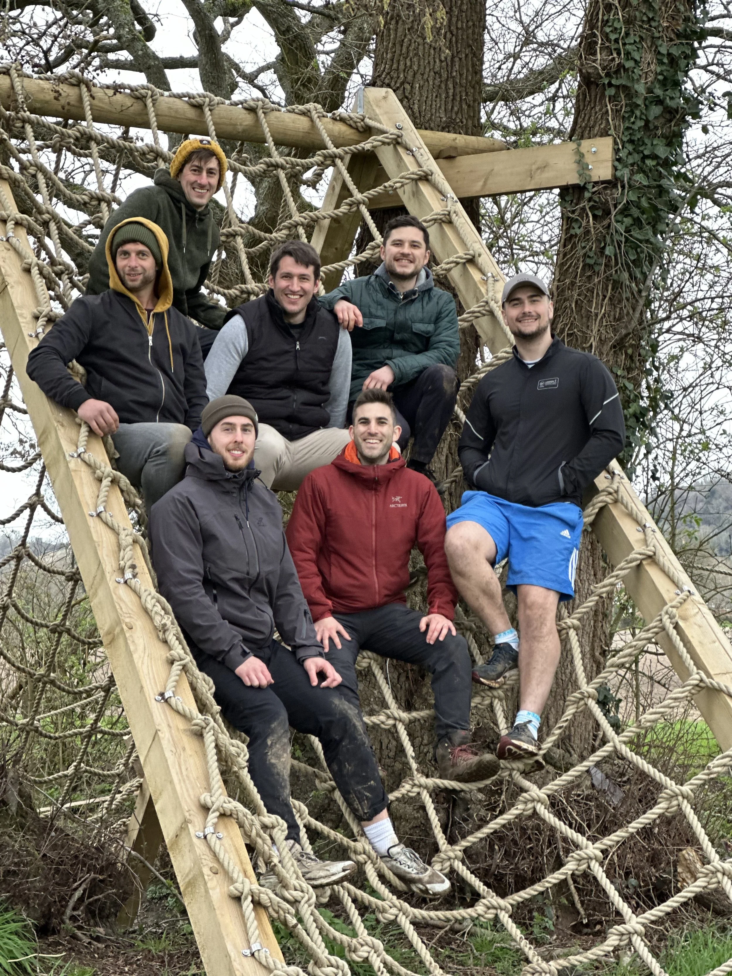 Group of eight young men posing on a wooden and rope climbing structure in a wooded outdoor area during daytime. Dr Matt Slavin, Clinical Psychologist
