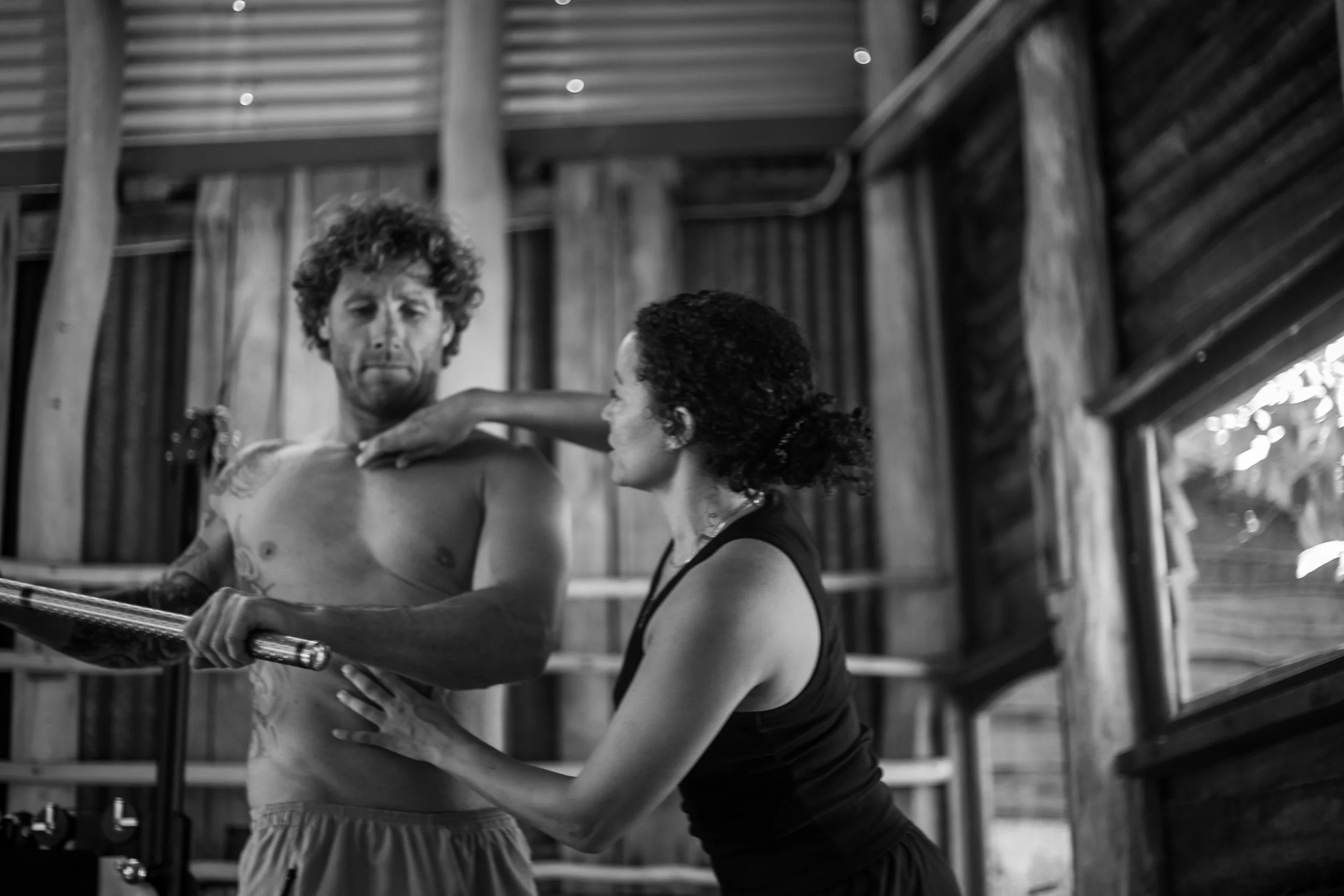 A man and a woman practicing martial arts with a wooden stick inside a wooden structure.