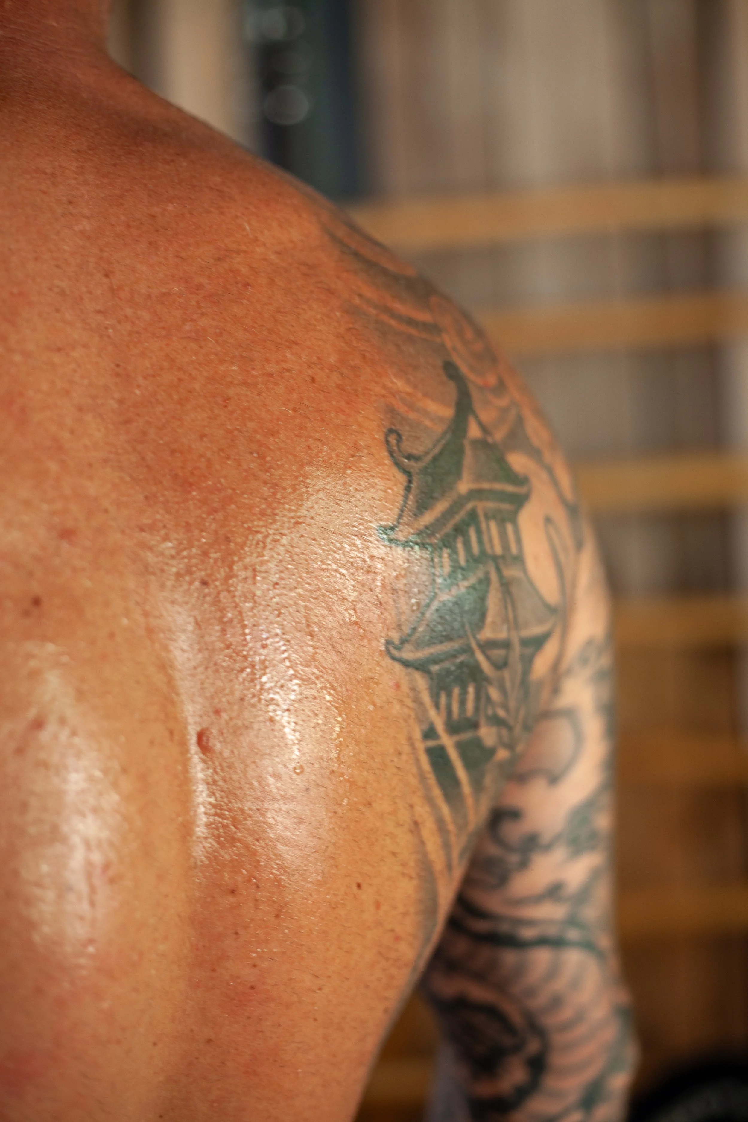 Close-up of a person's shoulder and upper arm showing tattoos, with a wooden background.